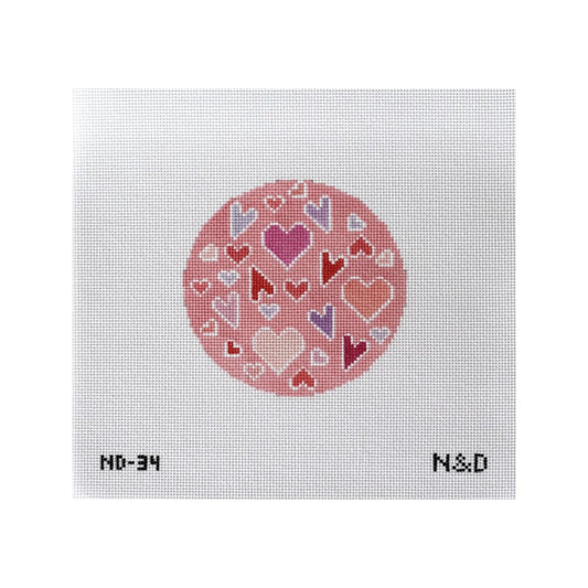 Cross-stitched pattern of hearts in a circle on fabric with 'N&D' branding.