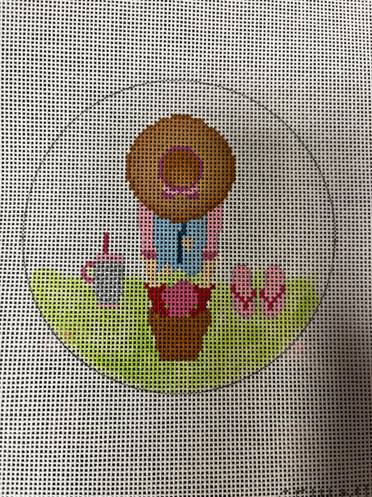 Cross-stitched design of a donut with a face, pink flowers, and a green base on a grid background.
