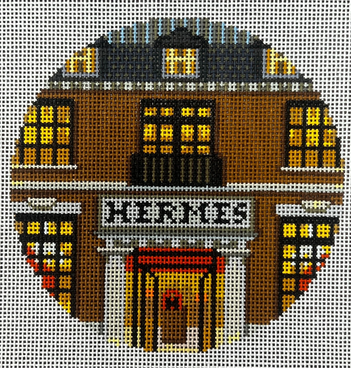 Decorative needlepoint of a building facade with 'HERMES' text