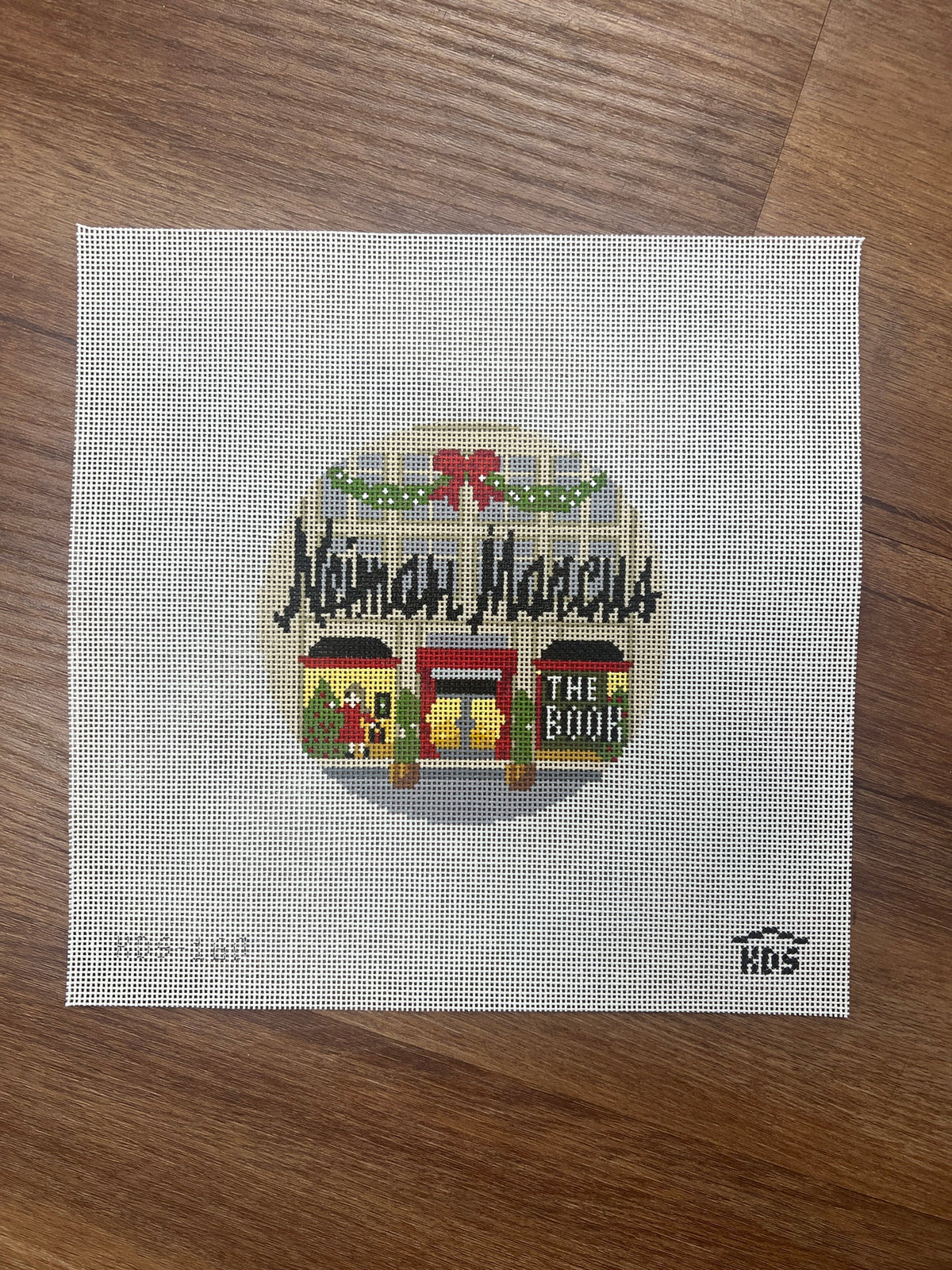 Cross-stitched design of a store front with 'Neiman Marcus' text on a wooden surface
