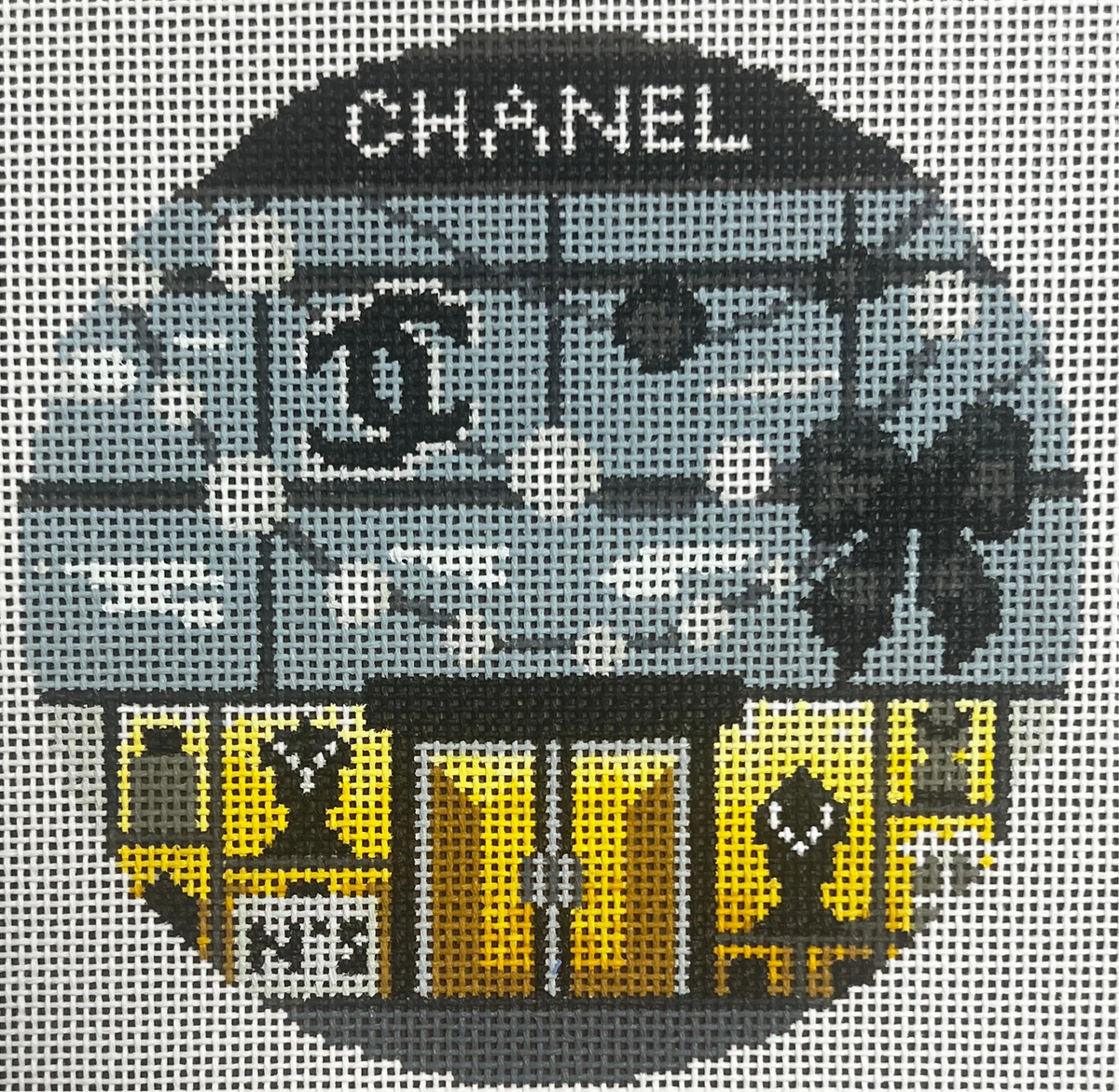 Decorative needlepoint of a Chanel store with palm trees and a car, featuring the brand's logo.