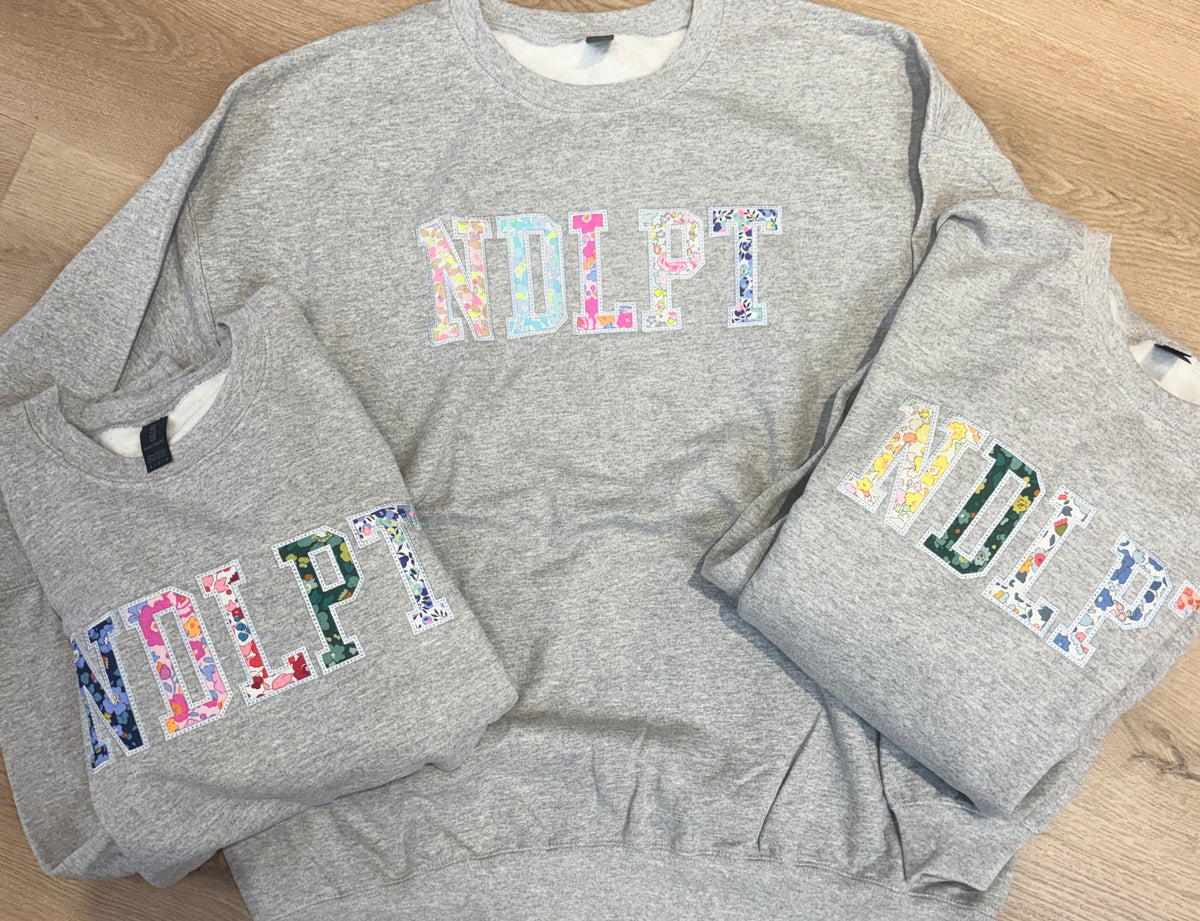 Three gray sweatshirts with colorful NDLPT floral design