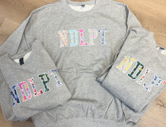 Three gray sweatshirts with colorful NDLPT floral design
