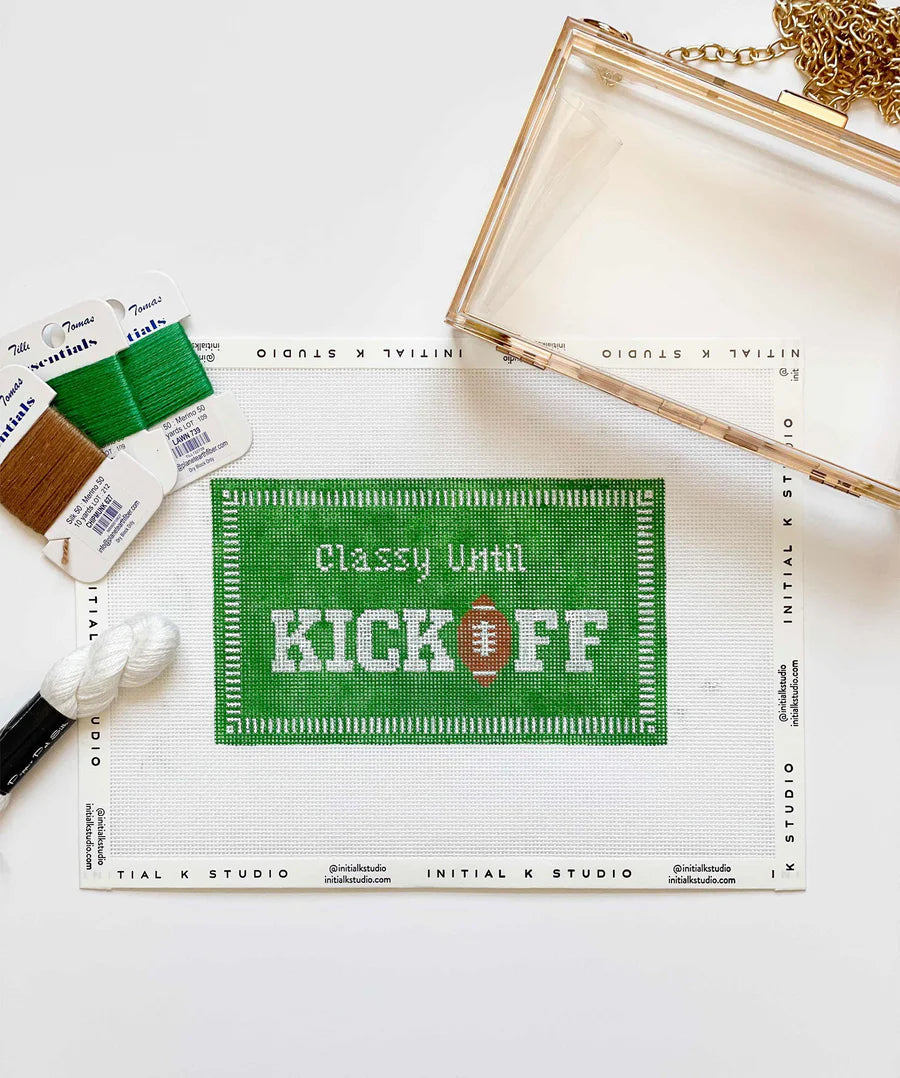 Cross-stitch kit with 'Classy Until Kick Off' design on a white surface with paint supplies.