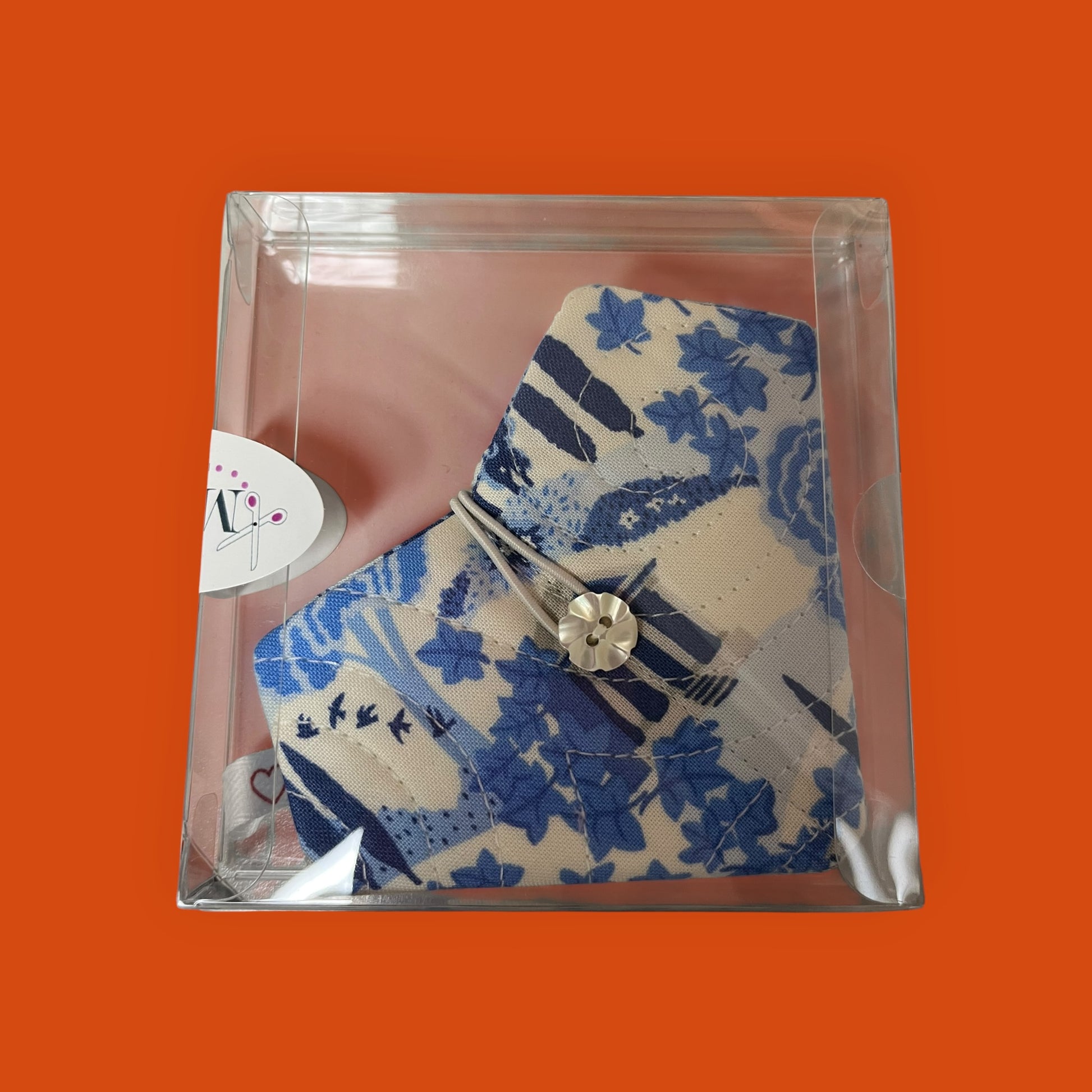 Blue floral-patterned product in clear packaging on an orange background