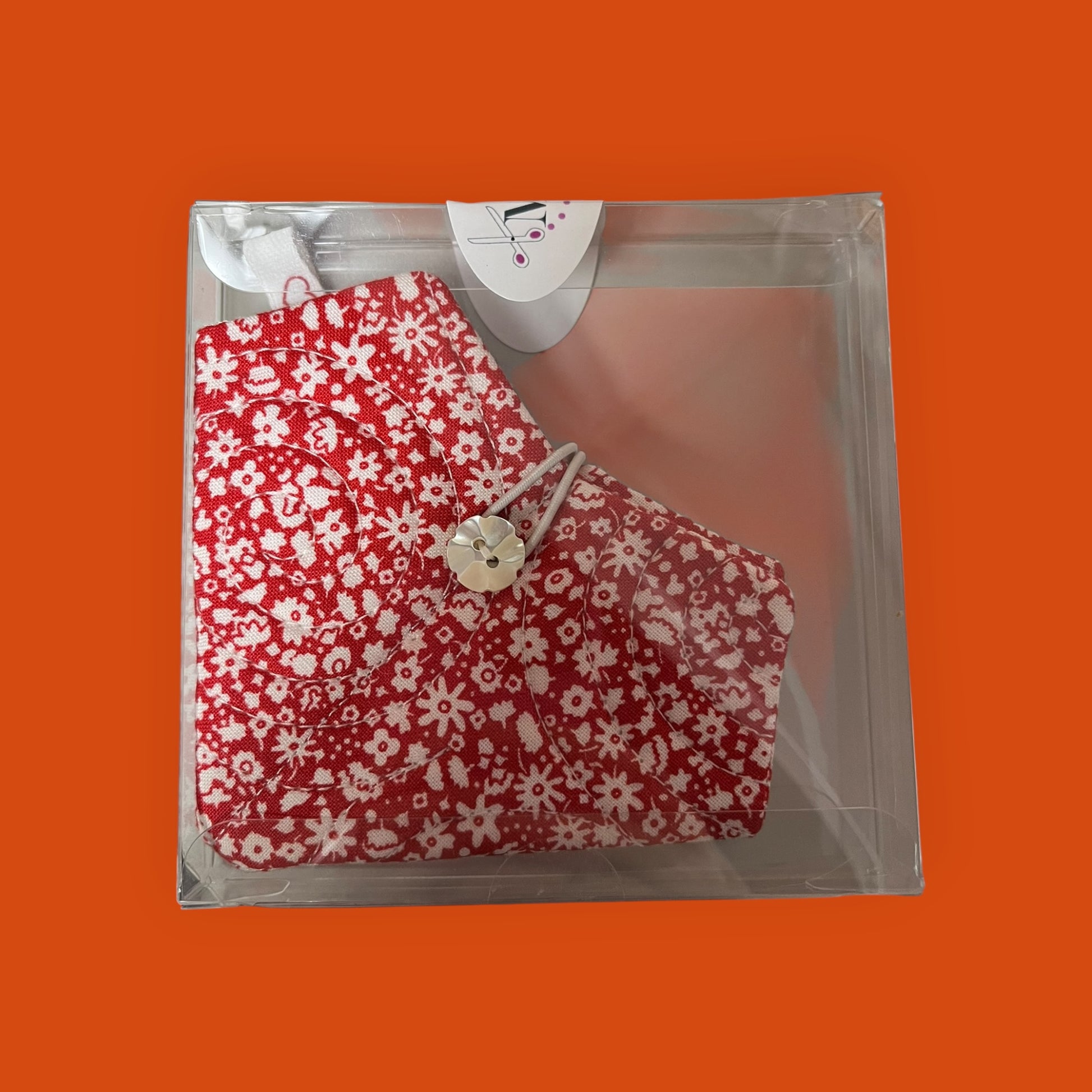red floral-patterned product in clear packaging on an orange background