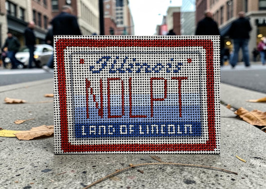 Small embroidered sign with 'NOLP' and 'Land of Lincoln' text on a city street background