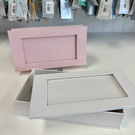 Two rectangular cardboard boxes, one pink and one gray, on a light surface with price tags in the background.