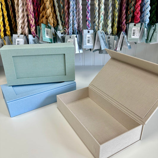 Open beige box with a light blue box and colorful yarn in the background.