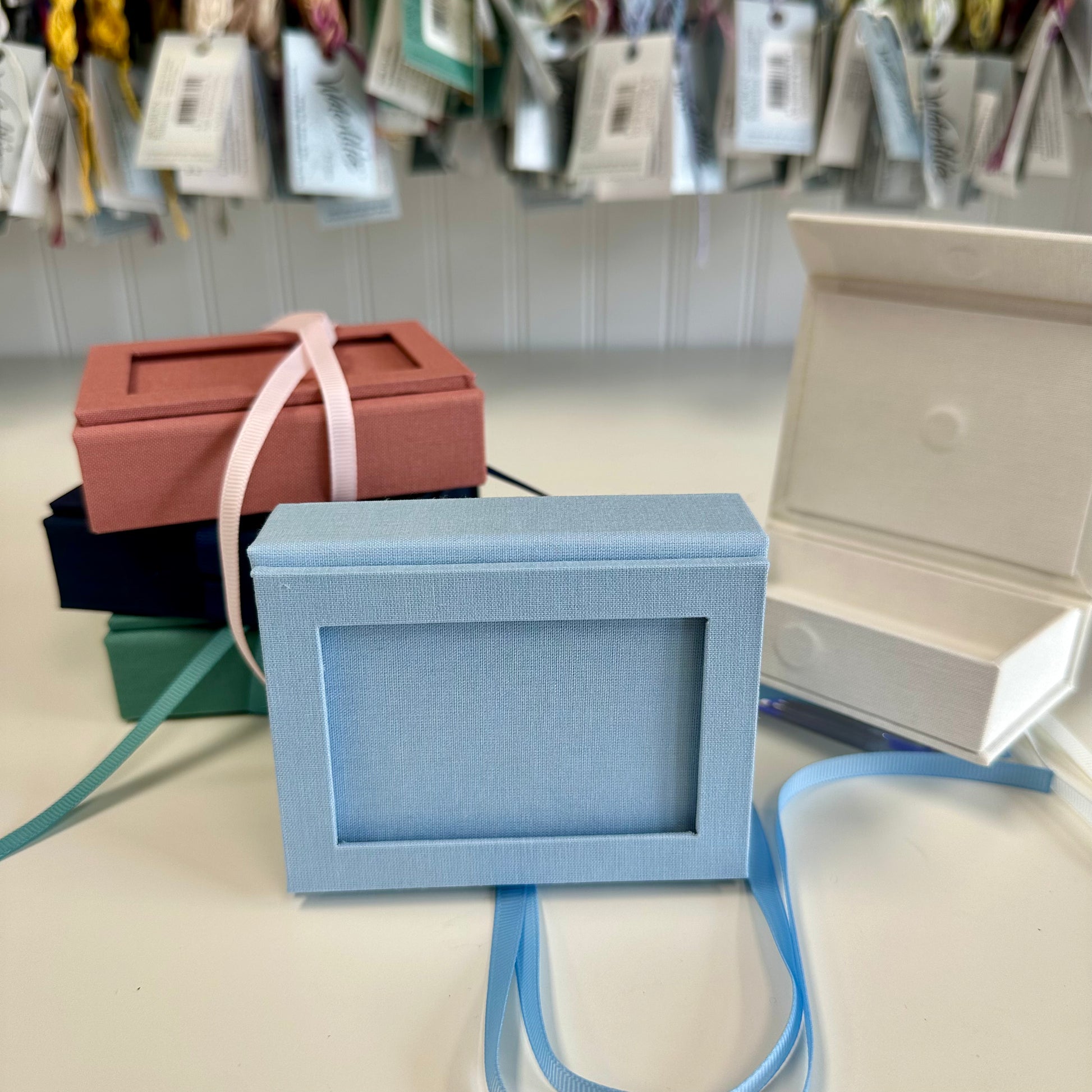 Blue jewelry box with a strap on a table, surrounded by other boxes and tags.