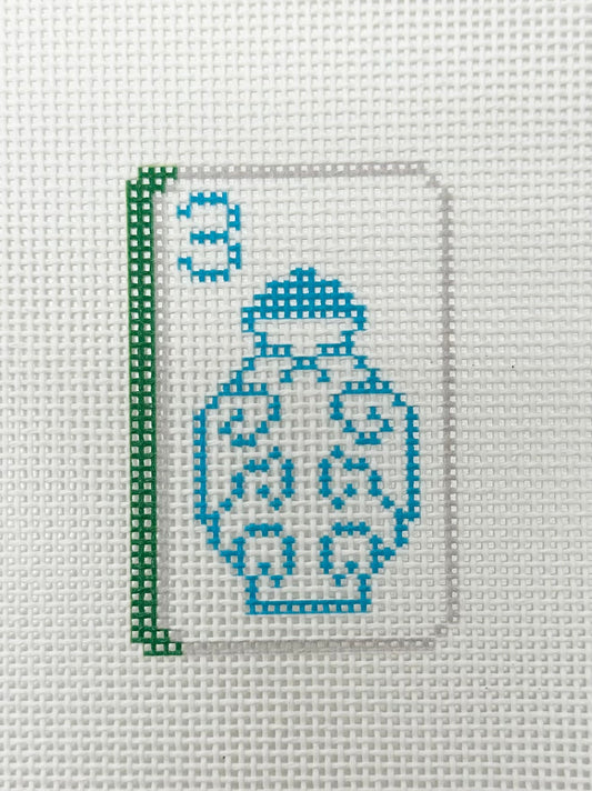 Cross-stitched design of a vase on fabric with a green border