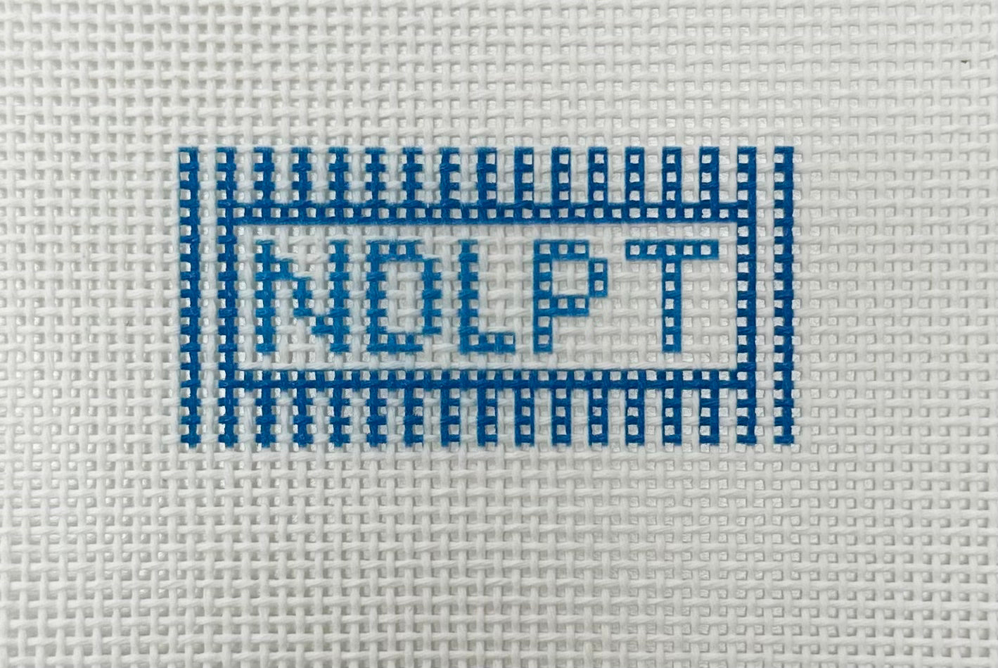Cross-stitched pattern of 'NDLPT' on a fabric background