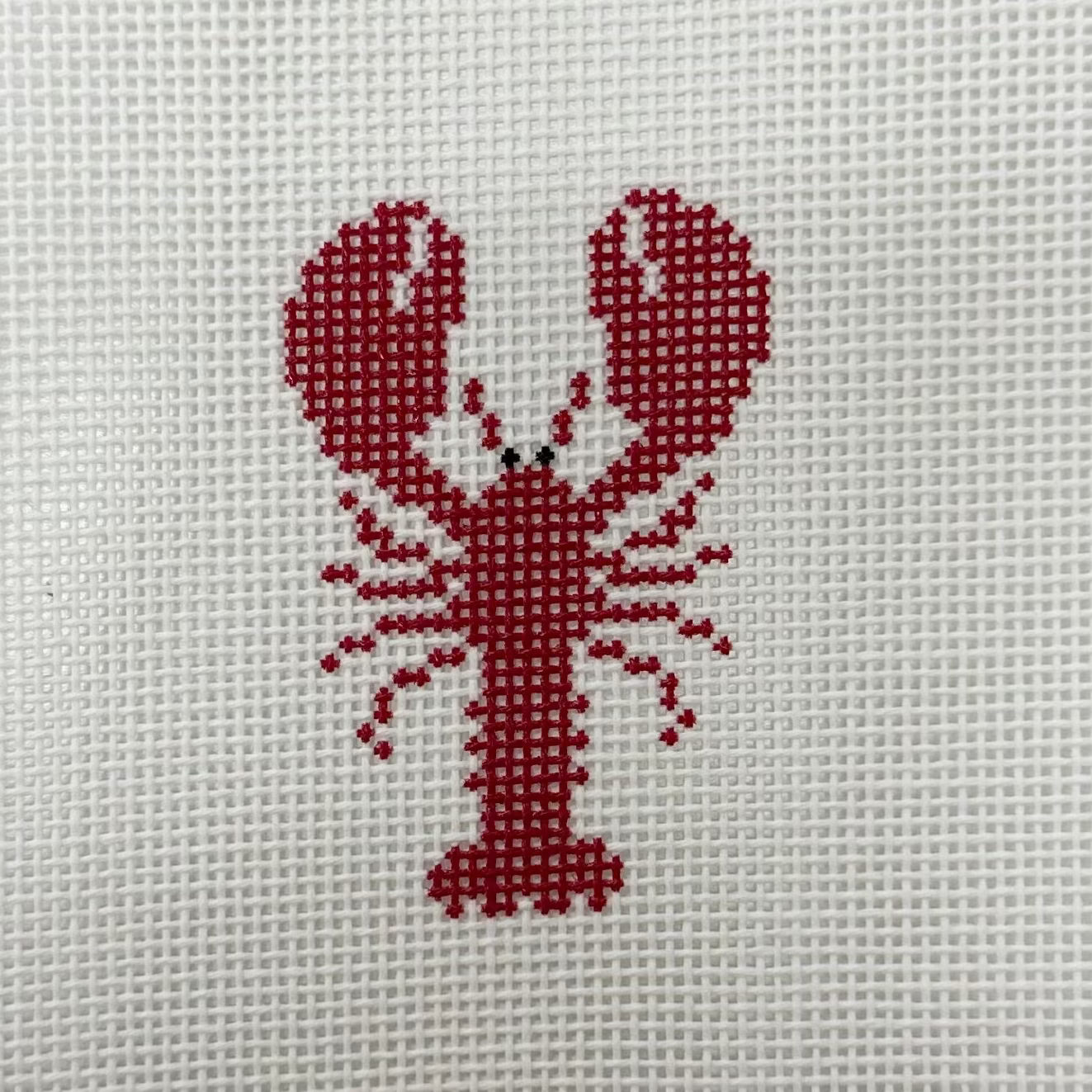 Cross-stitched red lobster on a white fabric background