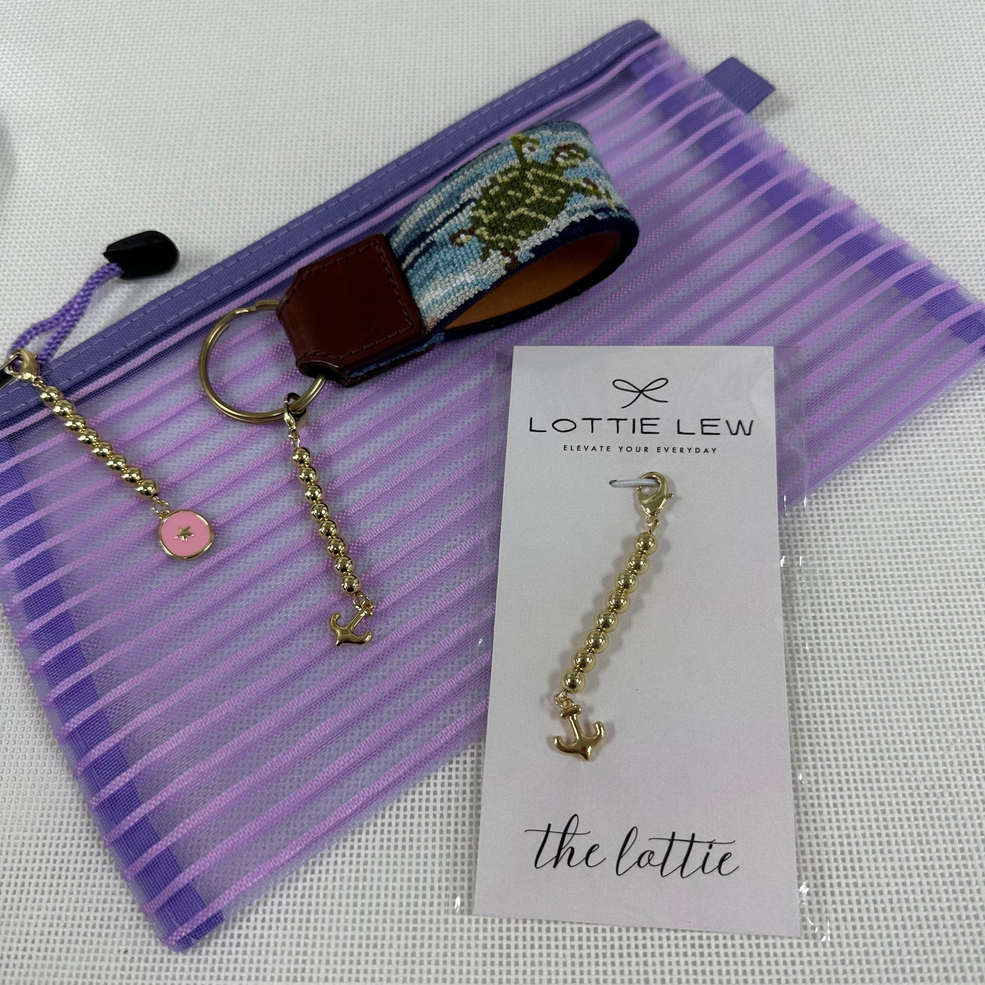 Gold keychain with pink charm on a purple pouch, accompanied by a Lottie Lew card.