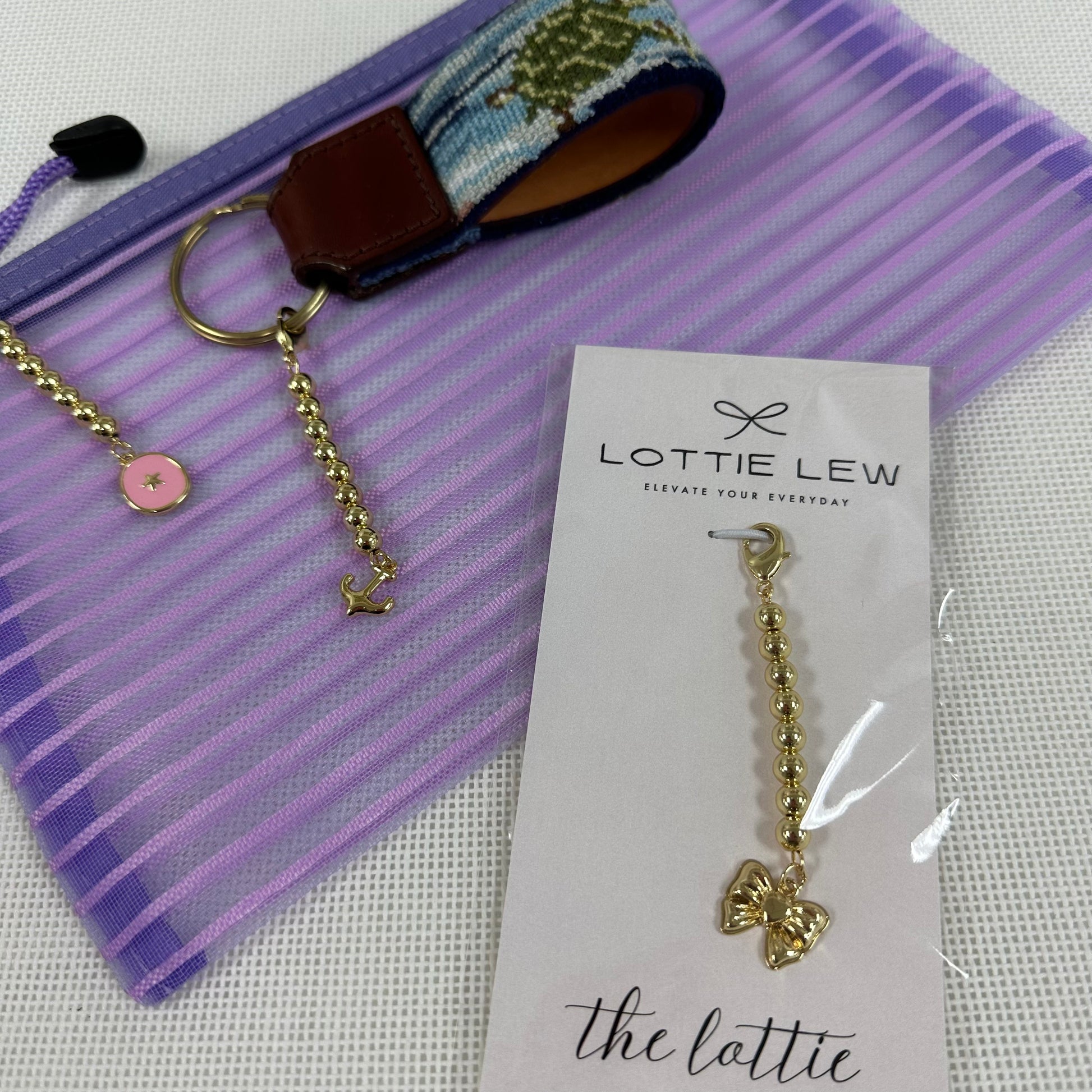 Gold keychain with pink charm on a purple striped background, featuring Lottie Lew branding.