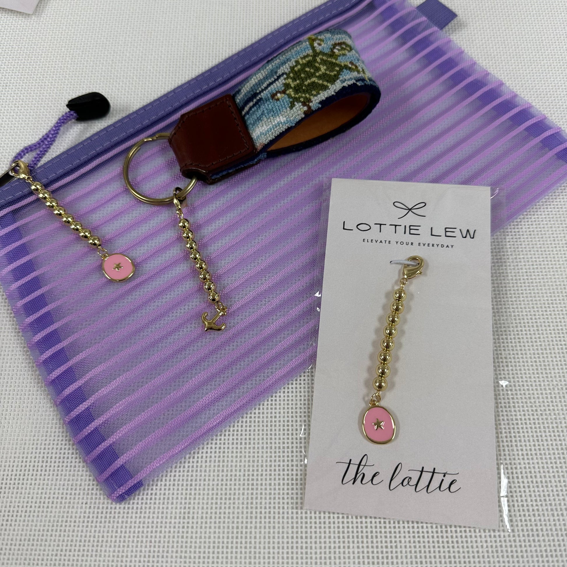 Keychain with pink charm and gold chain on a purple pouch with Lottie Lew branding.
