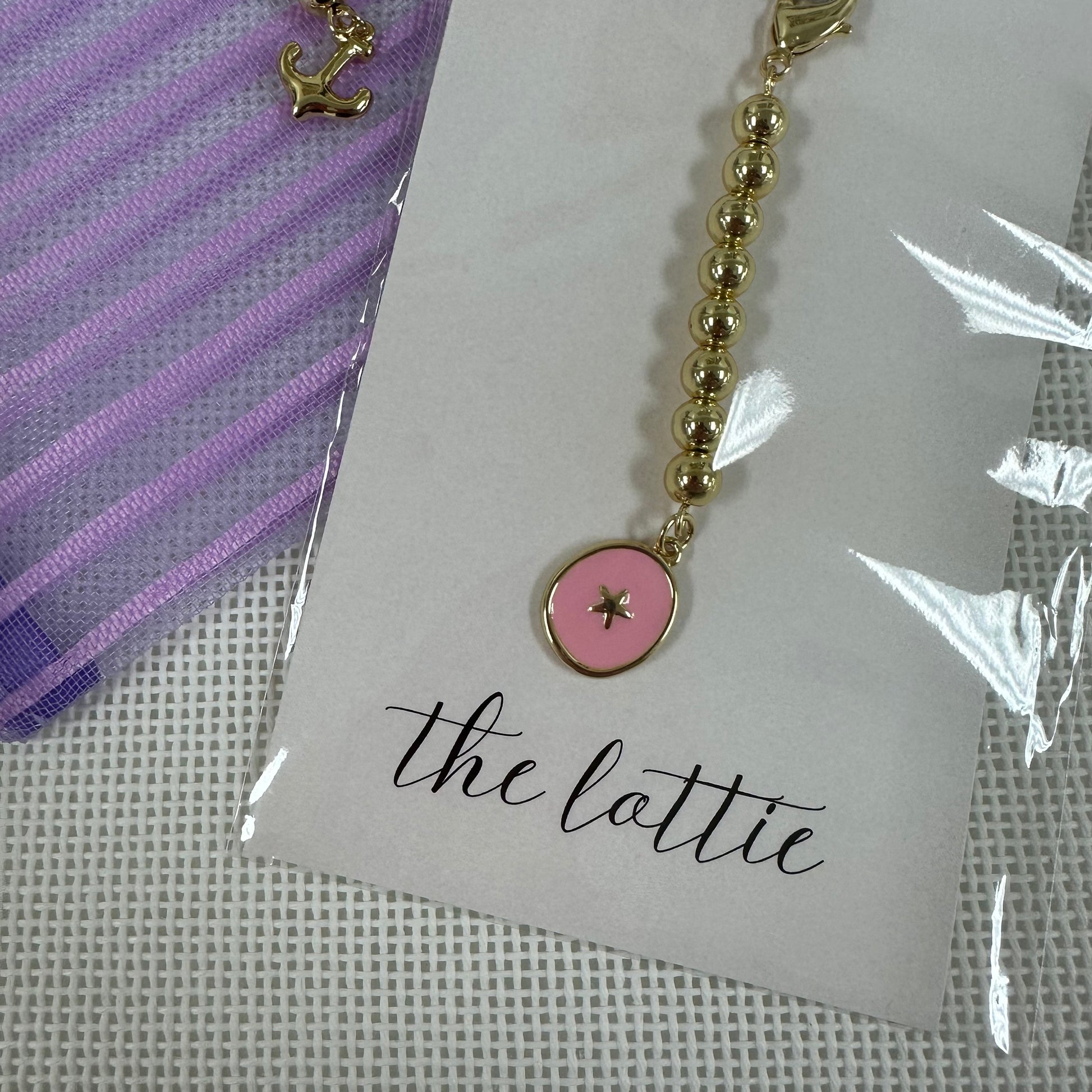 Gold beaded charm with a pink pendant on a card labeled 'the lattie' 