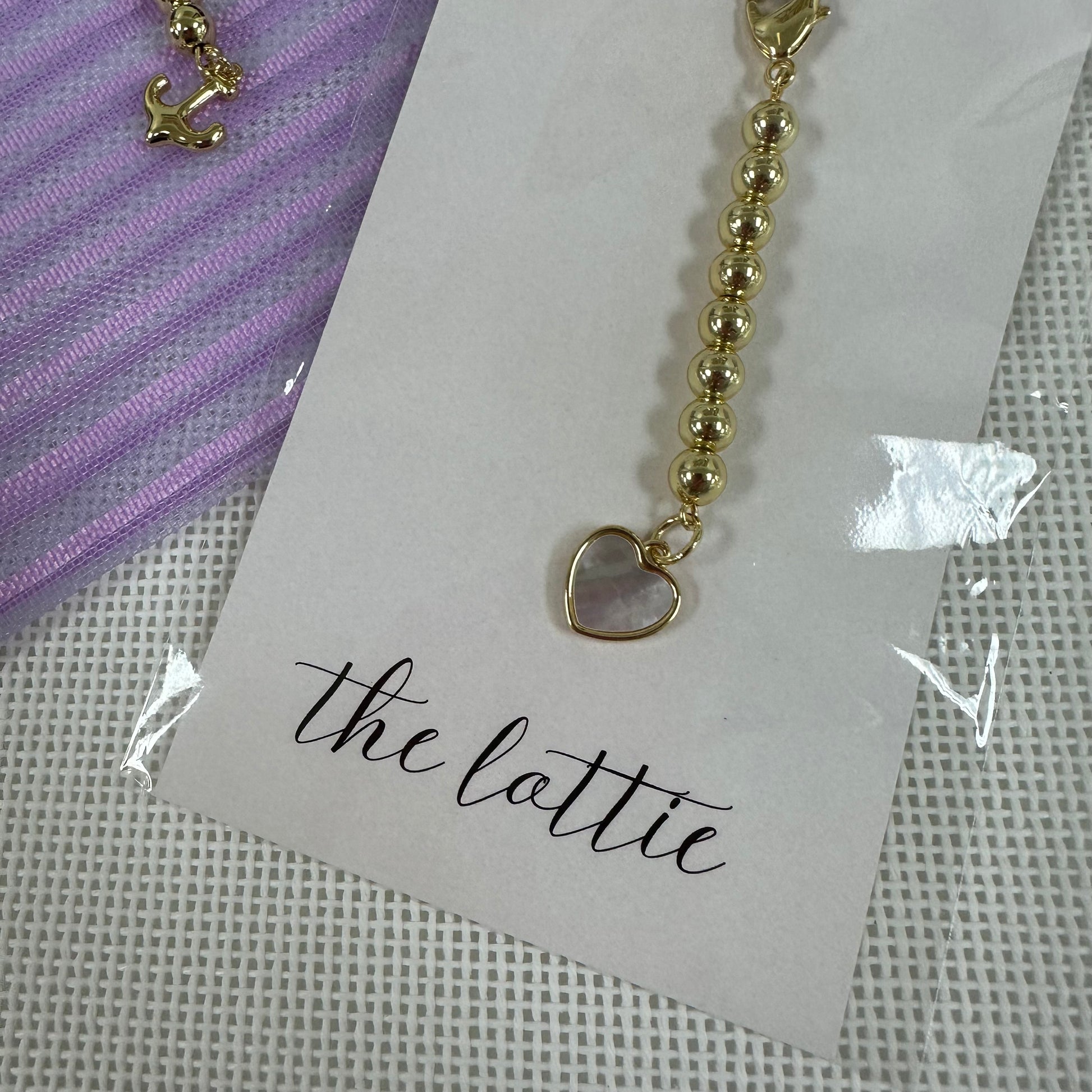 Gold charm with a heart pendant on a 'the lattie' branded card.