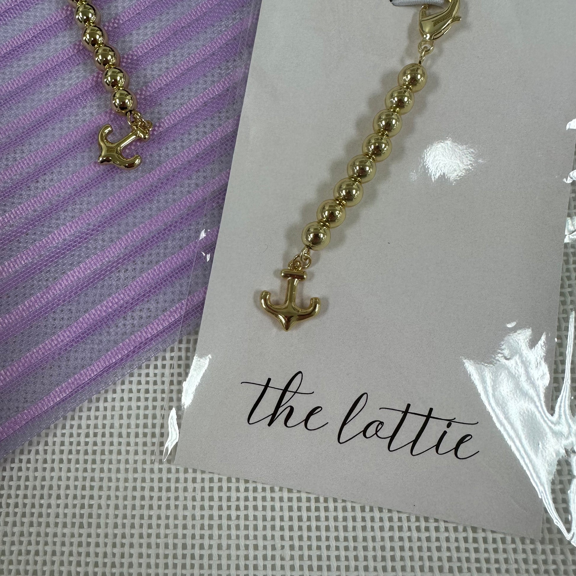 Gold beaded charm on a card labeled 'the lattie' against a purple and white striped background.