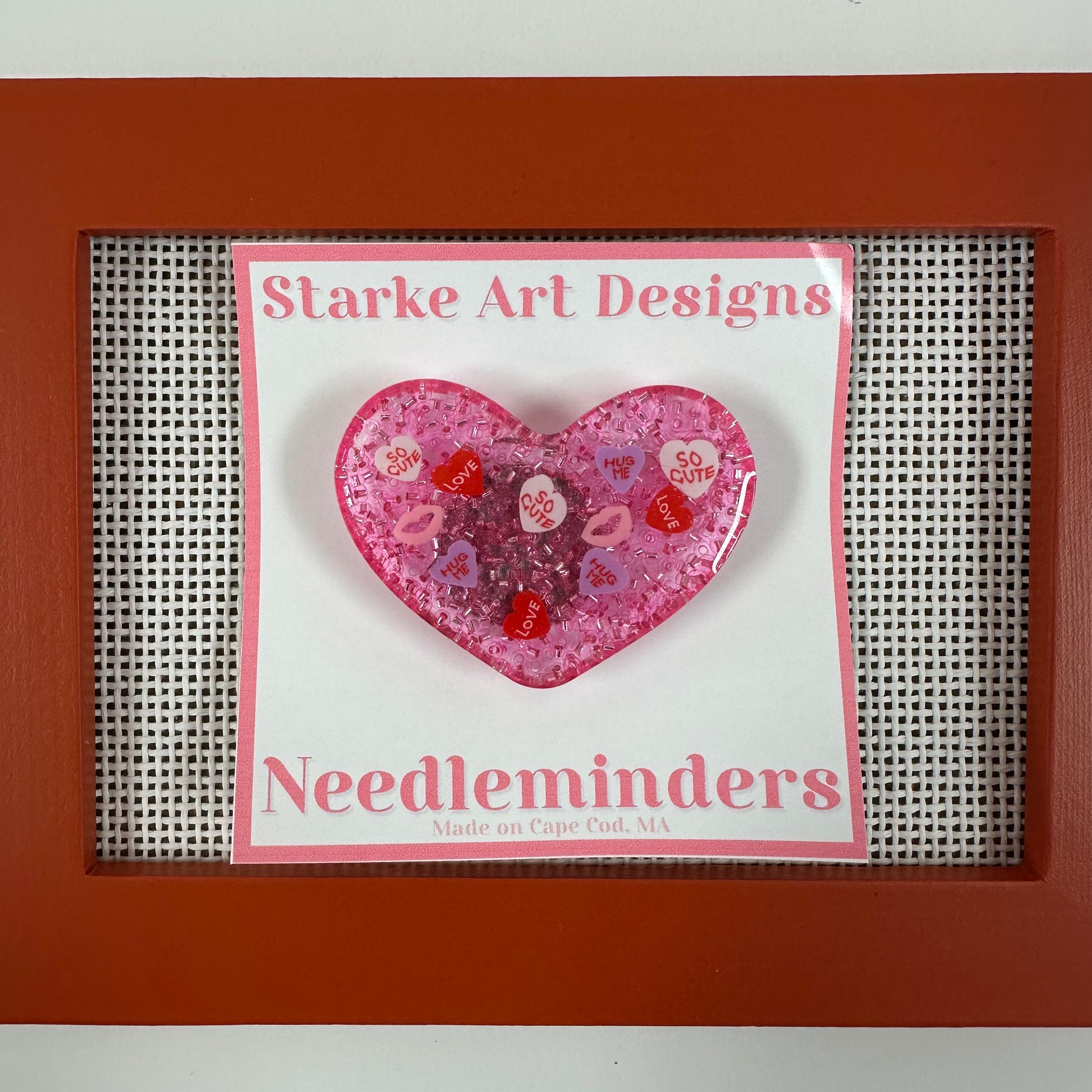 Pink heart-shaped needle minder with 'Starke Art Designs' branding on a white background