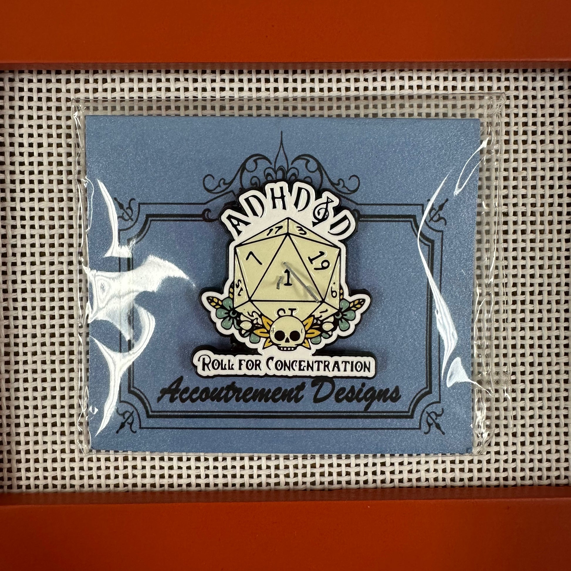 Decorative die with 'Accoutrement Designs' branding on a blue card with clear plastic wrap.