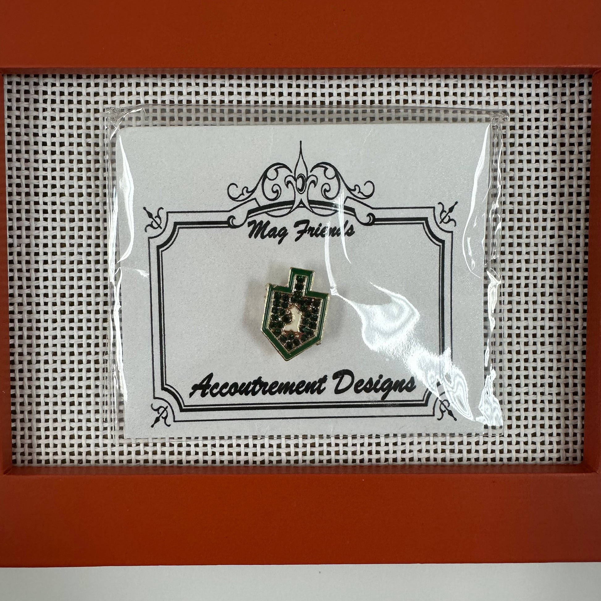 Pin on a card with 'Accoutrement Designs' branding, framed in red.
