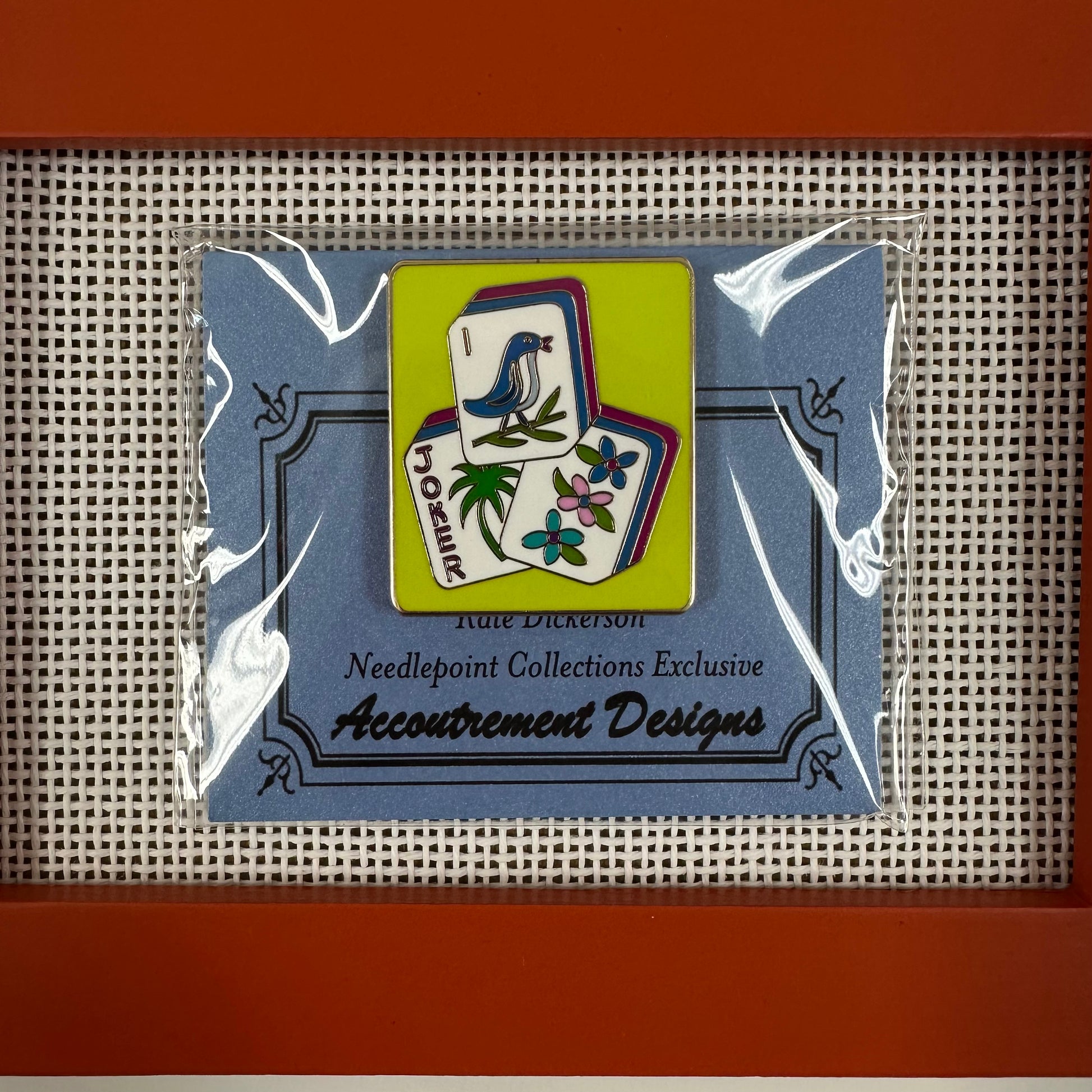 Pin with decorative design on a clear card, framed by a red border.
