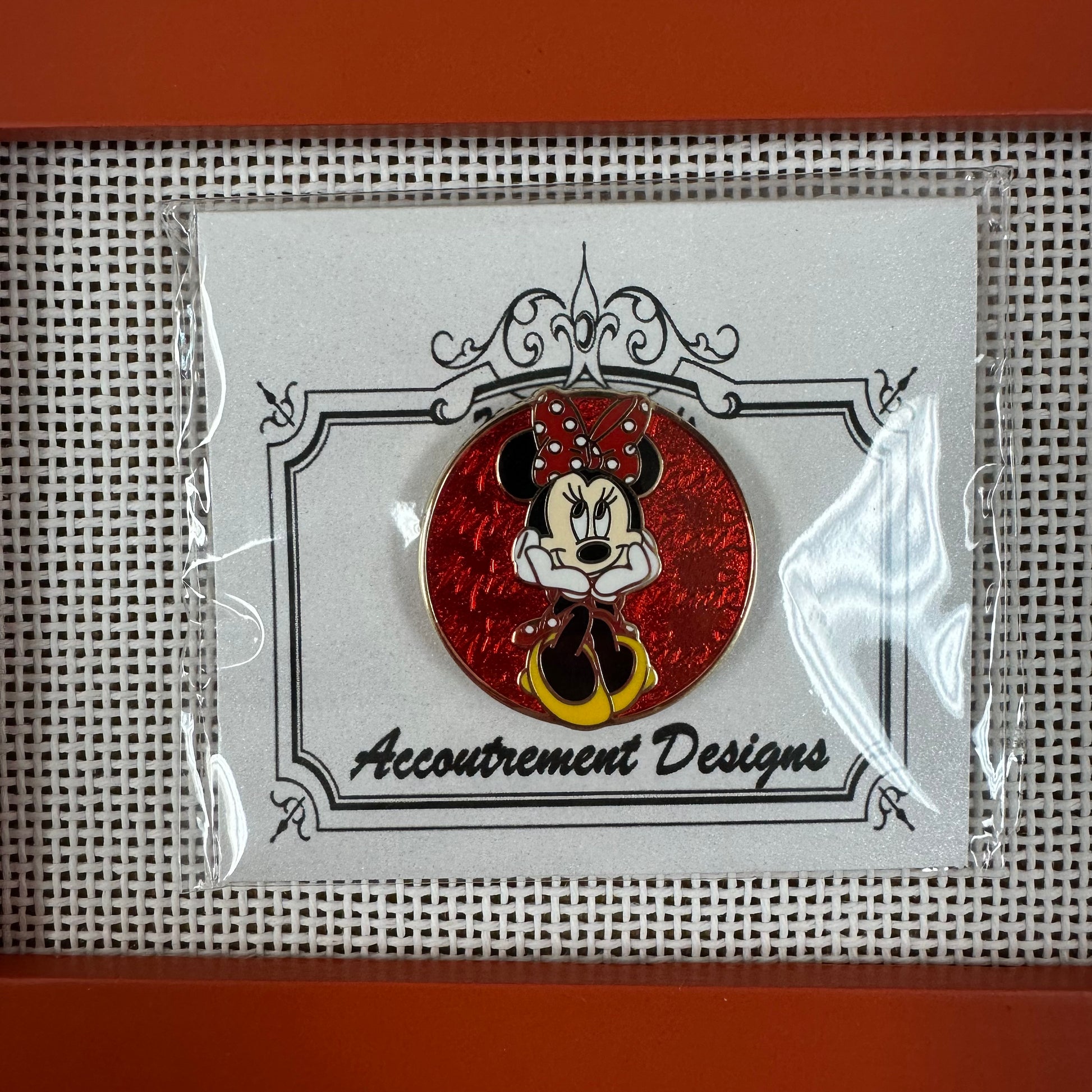 Minnie Mouse pin in clear packaging with 'Accoutrement Designs' label on a grid background