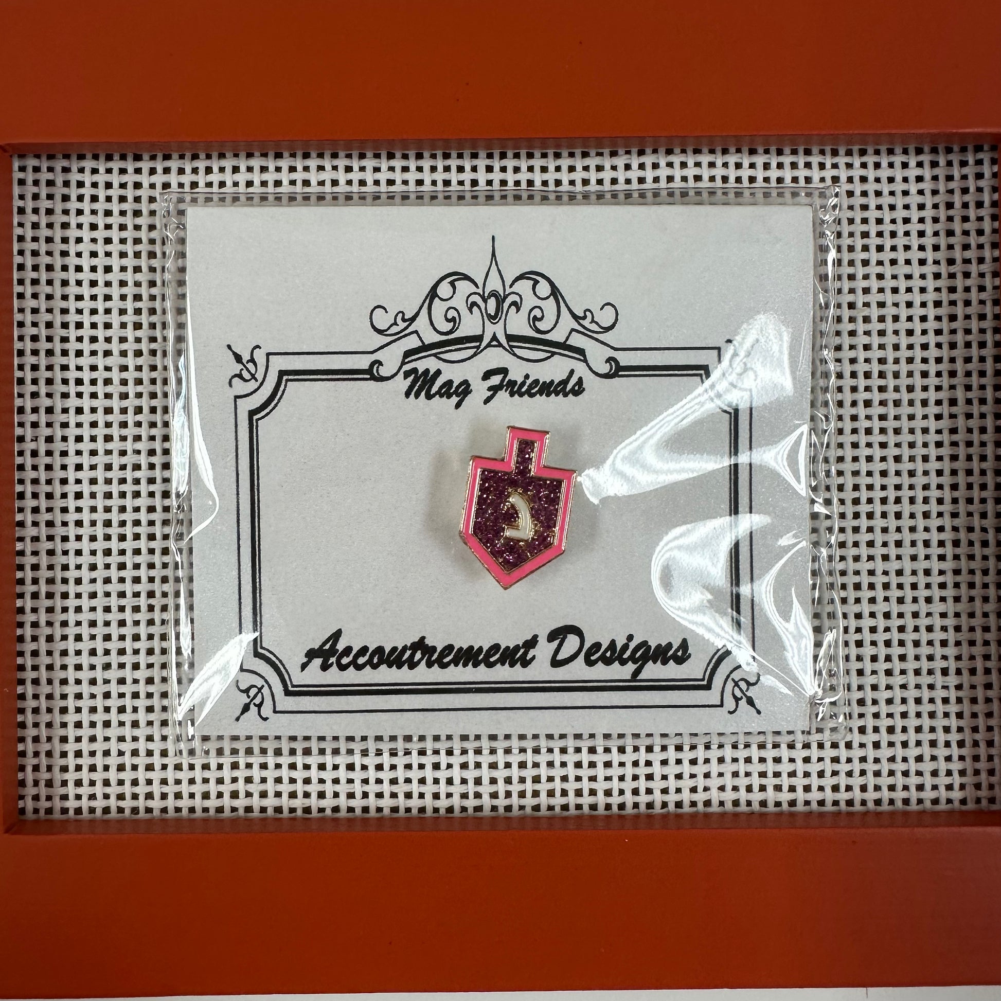Pin on a card with 'Accoutrement Designs' branding, displayed against a textured background.