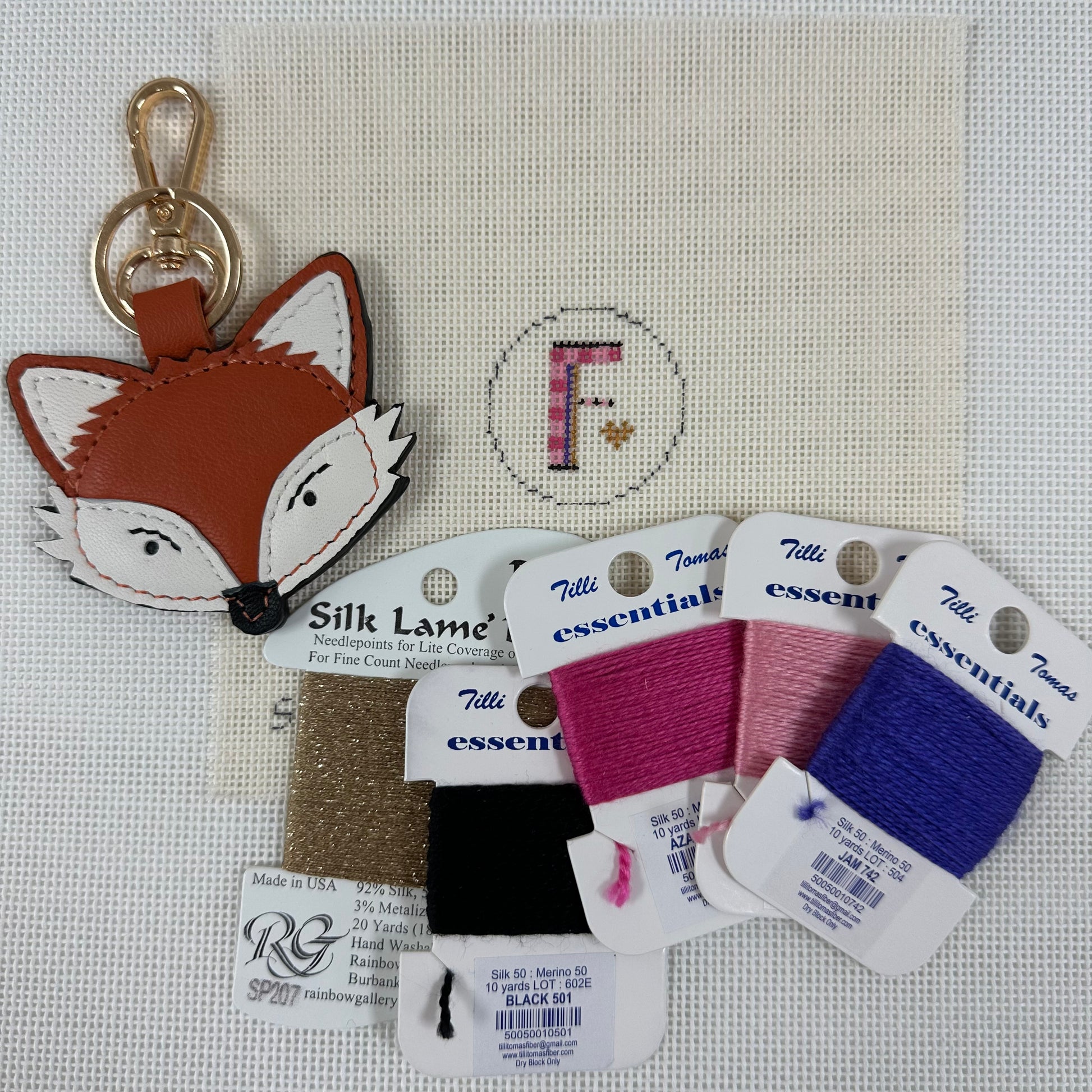 Fox-shaped keychain with Tilly's embroidery thread packages on a cross-stitched background