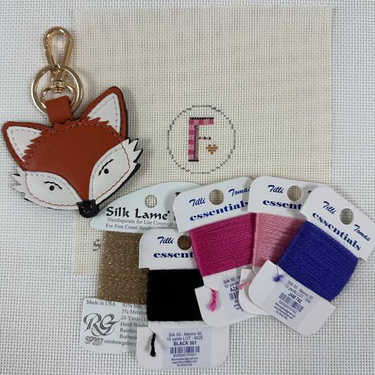 Fox-shaped keychain with Tilly's embroidery thread packages on a cross-stitched background