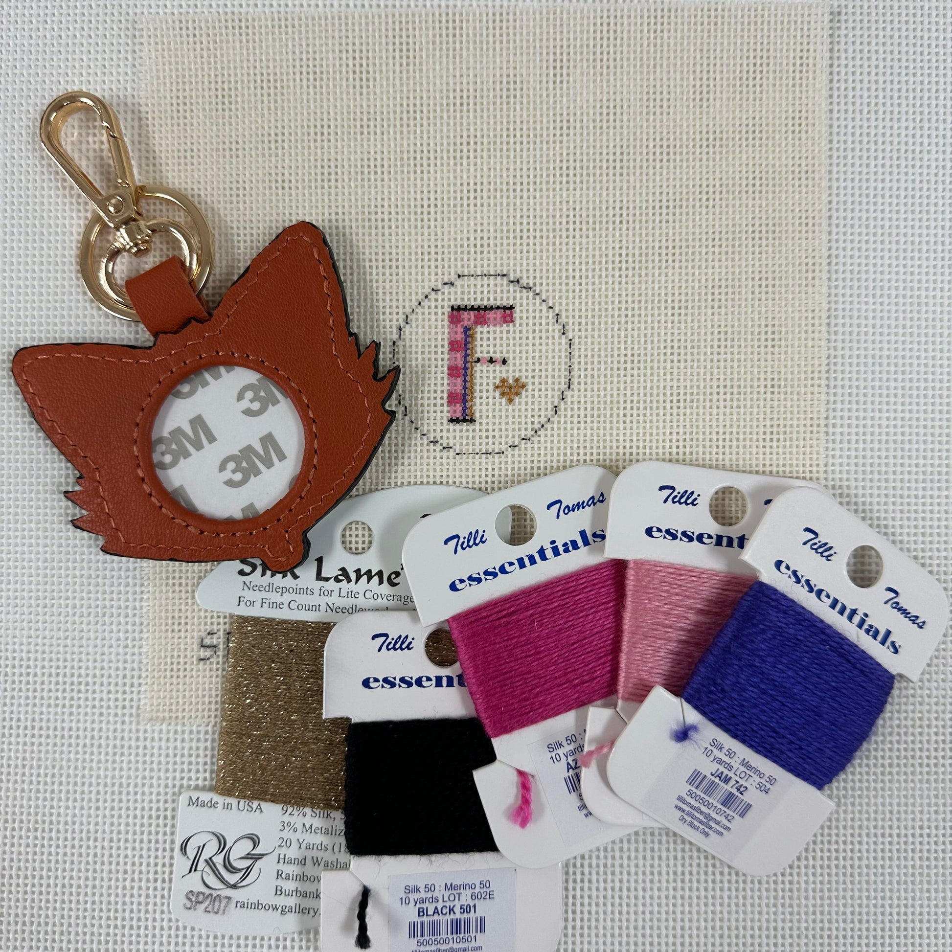 Keychain with mirror, thread spools, and labels on a textured fabric background