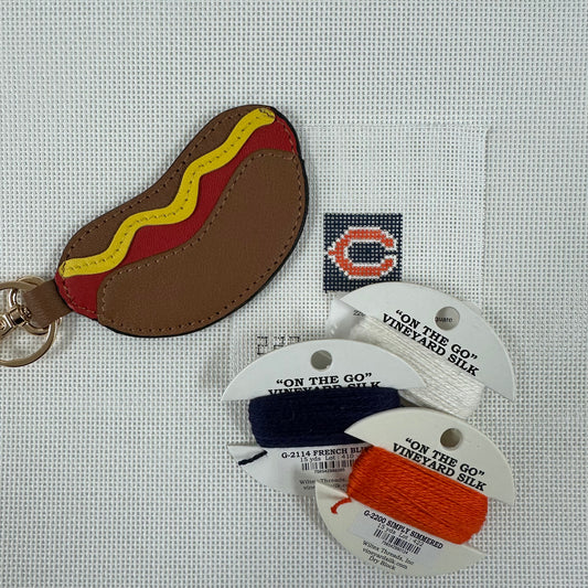 Hot dog-shaped keychain with 'On the Go' yarn packages on a textured surface
