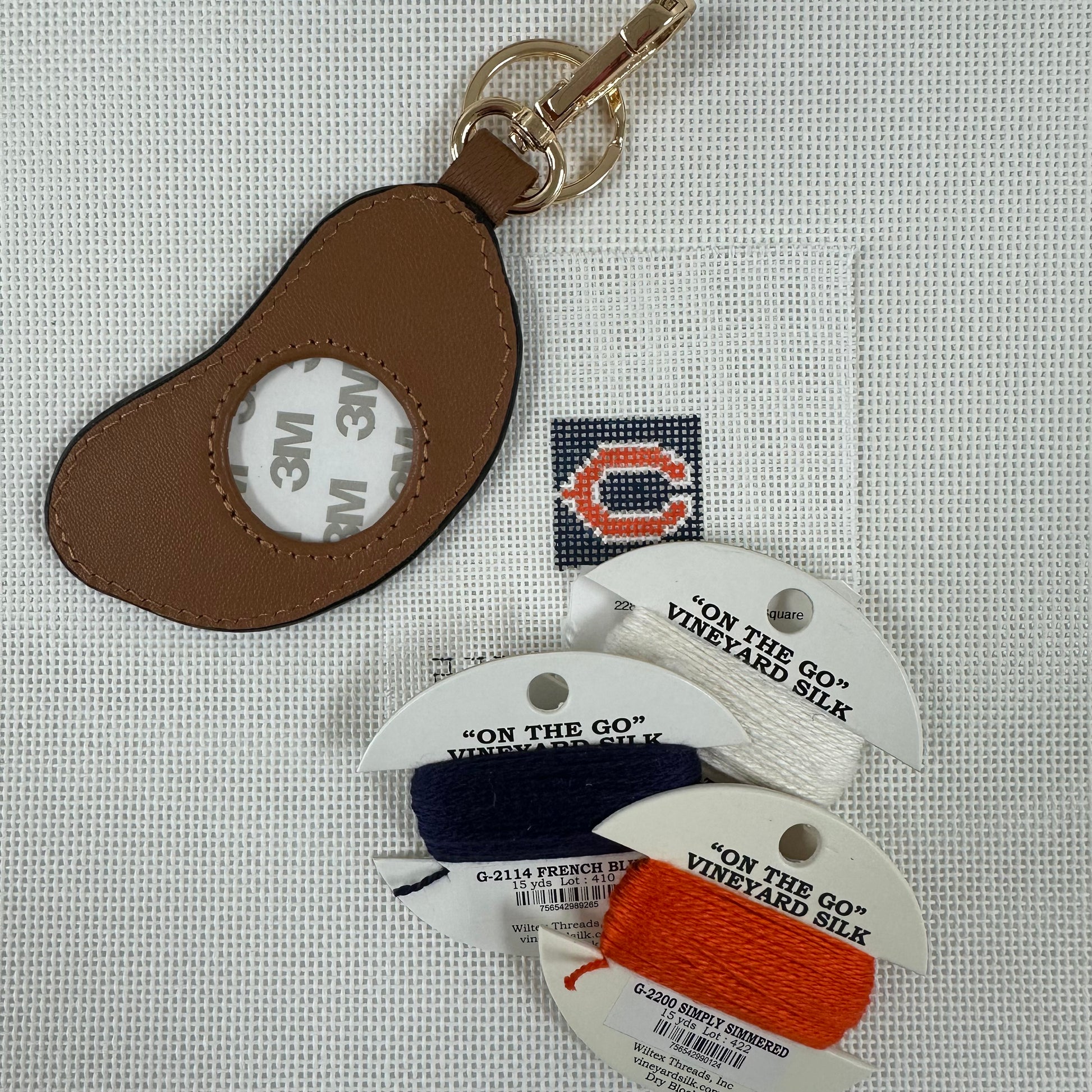 Brown leather keychain with 3M label, 'On the Go' thread labels, and spools of thread.