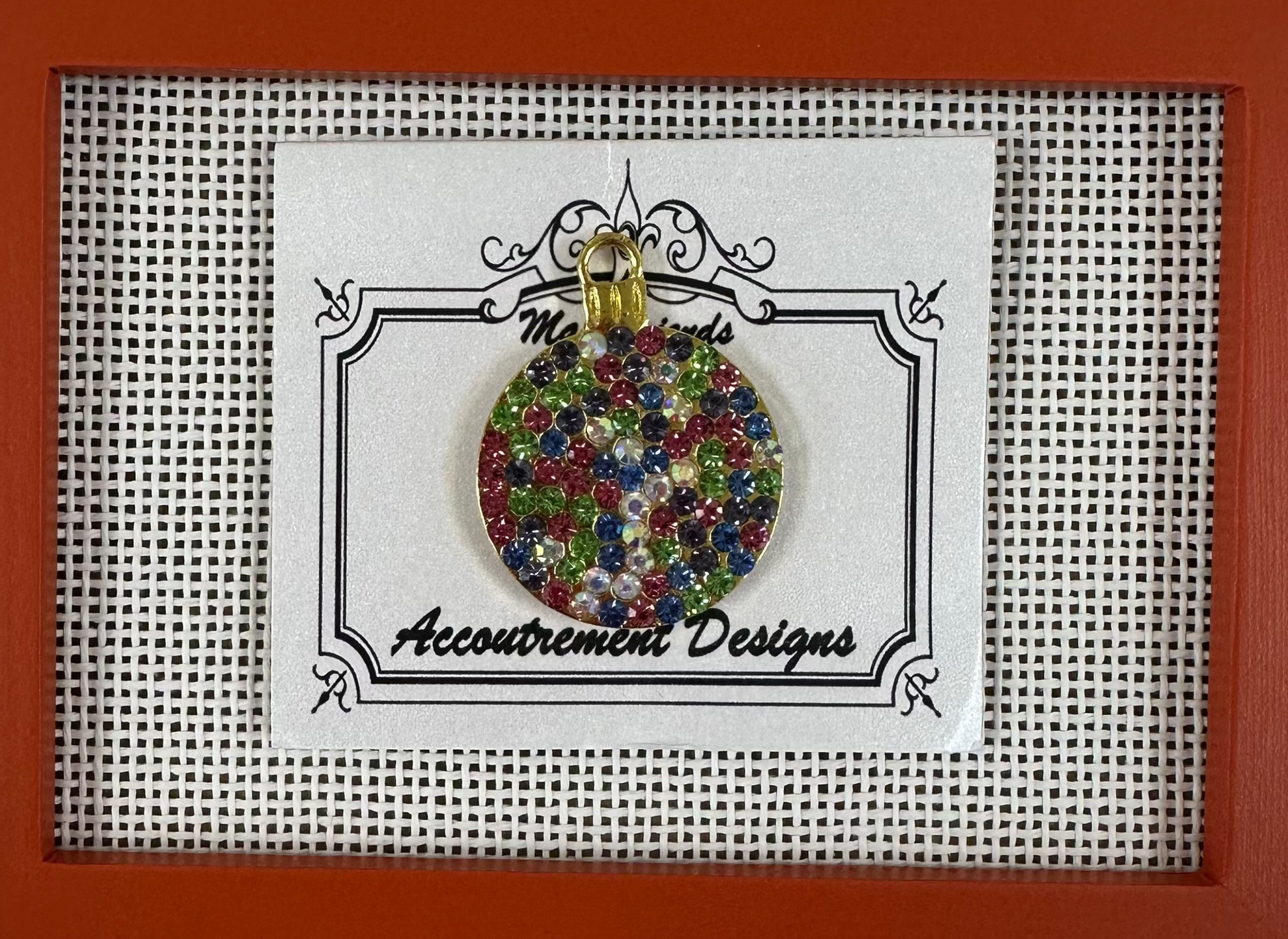 Colorful round pendant on a card with 'Accoutrement Designs' branding, framed in red.