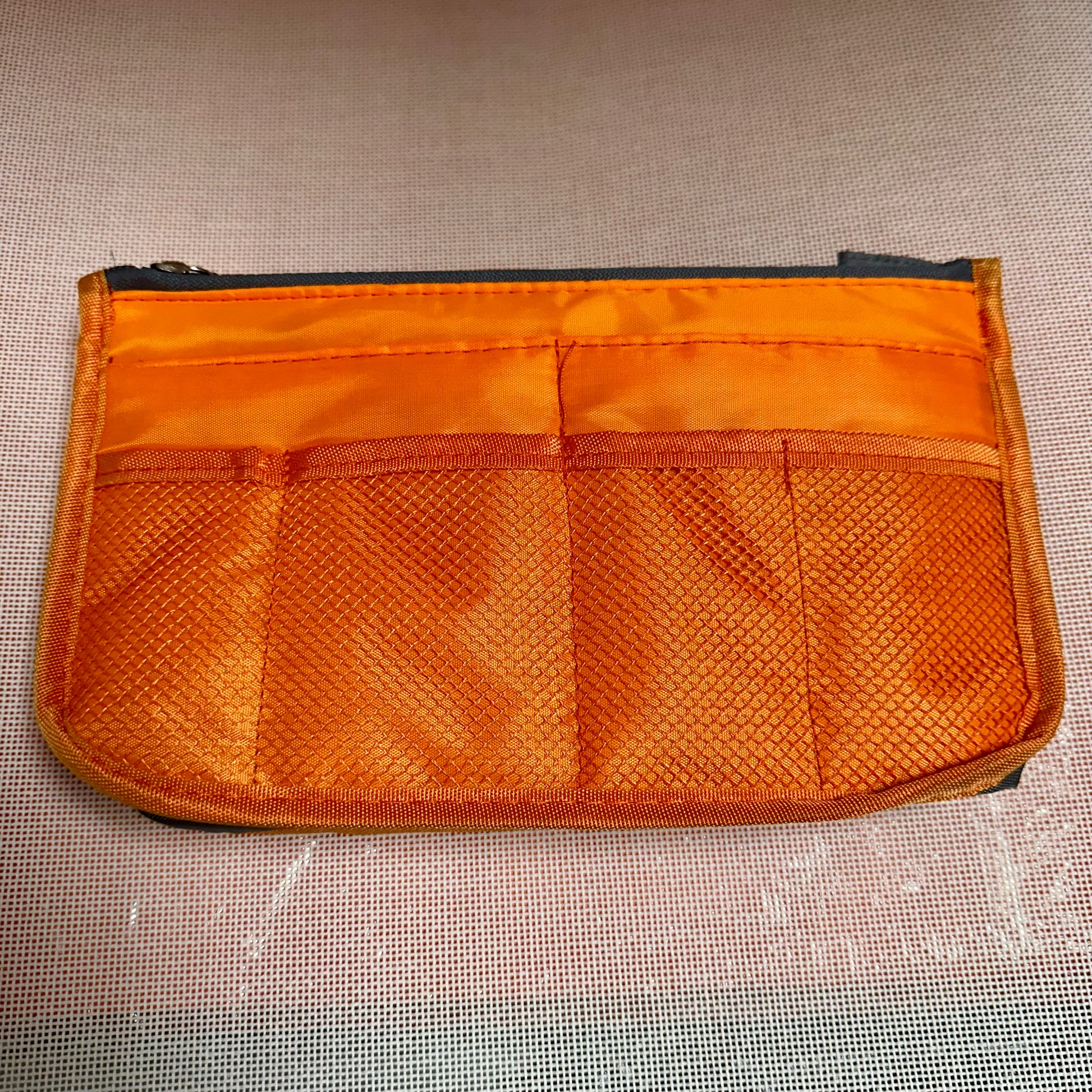Orange pouch with mesh pockets on a textured surface