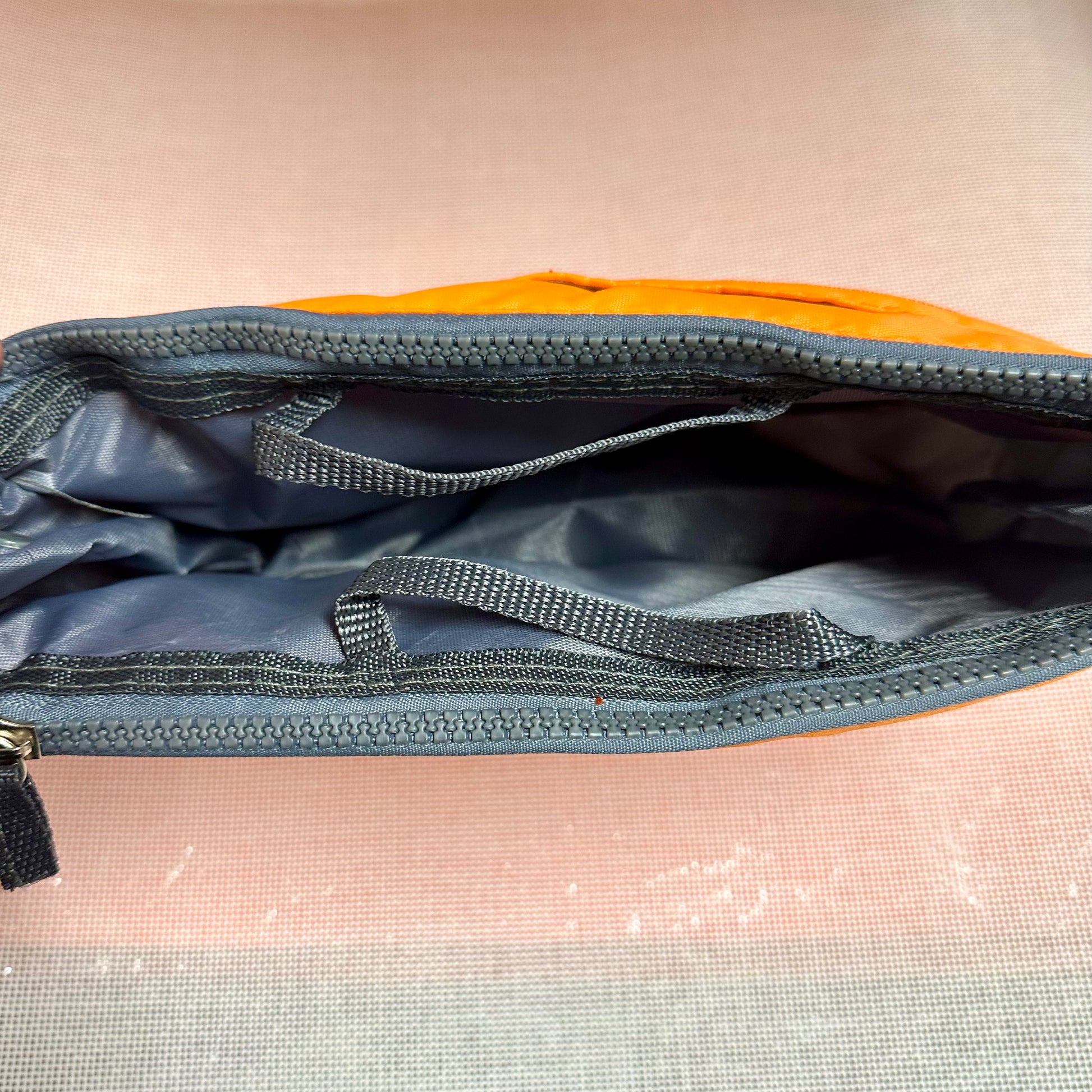 Close-up of a partially open blue and orange bag on a light pink surface.