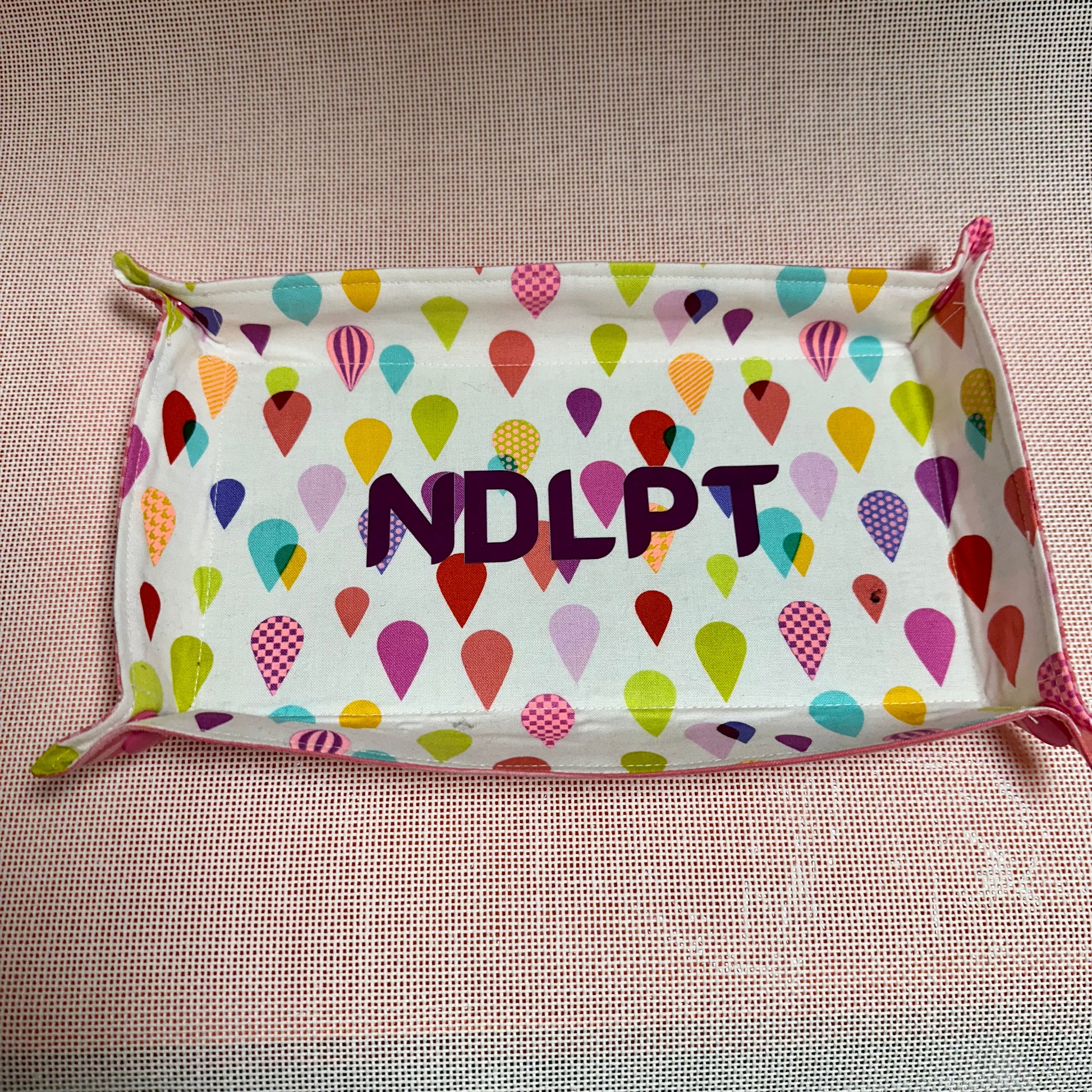 Fabric pouch with colorful heart pattern and 'NDLPT' text on a textured surface