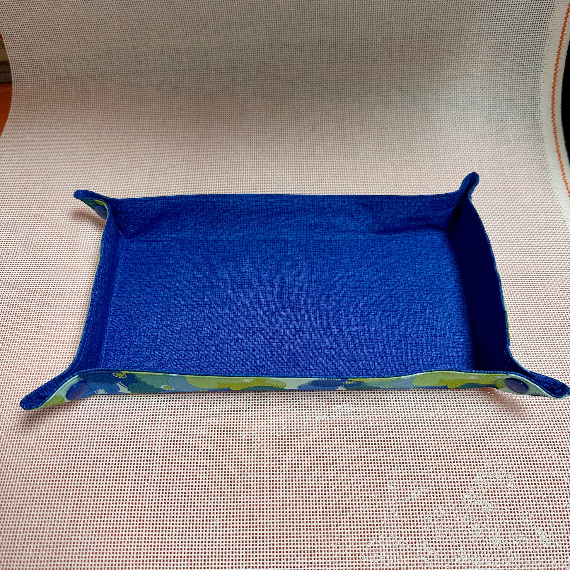 Blue fabric tray with green trim on a beige surface