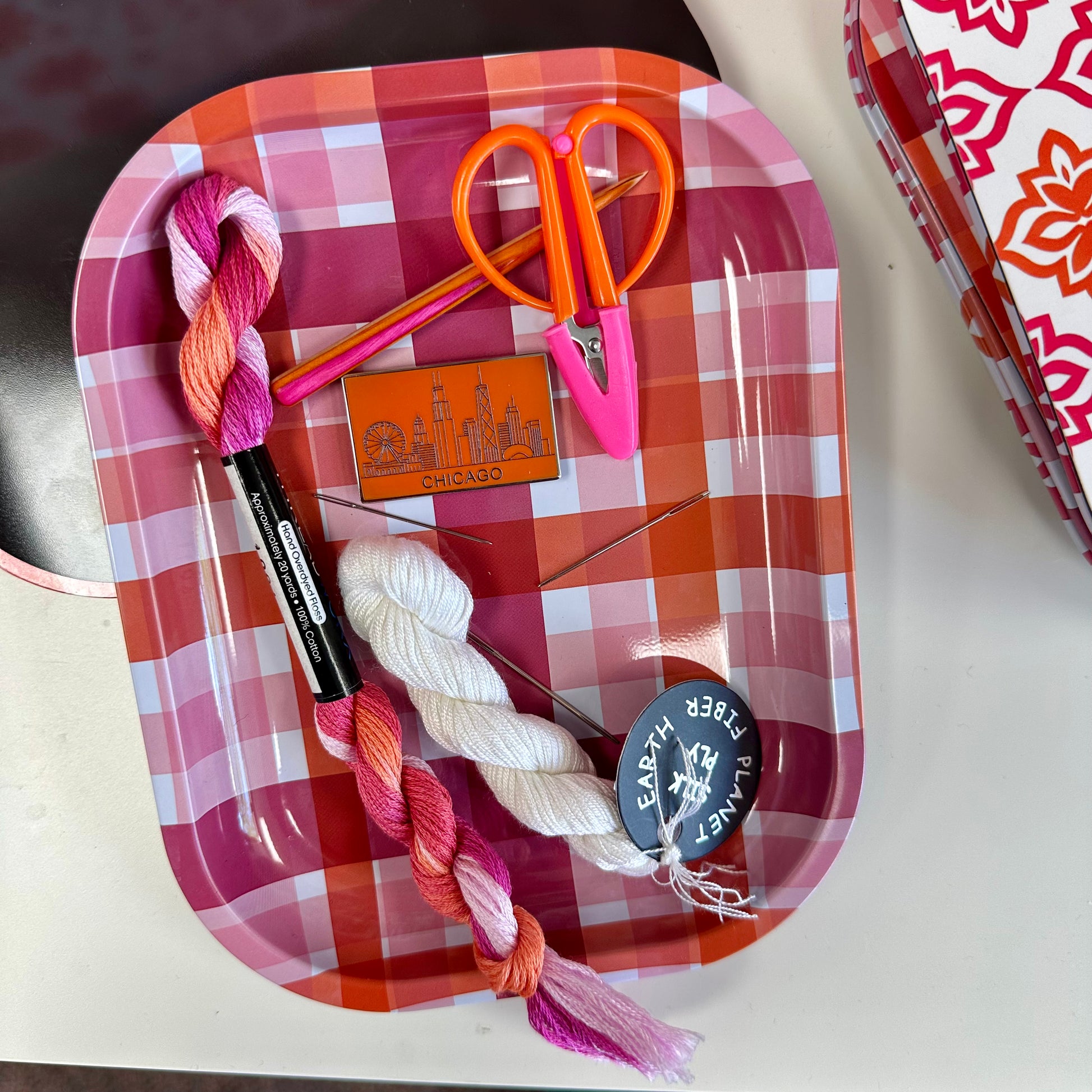 Red checkered tray with yarn, scissors, and a Chicago magnet on a white surface