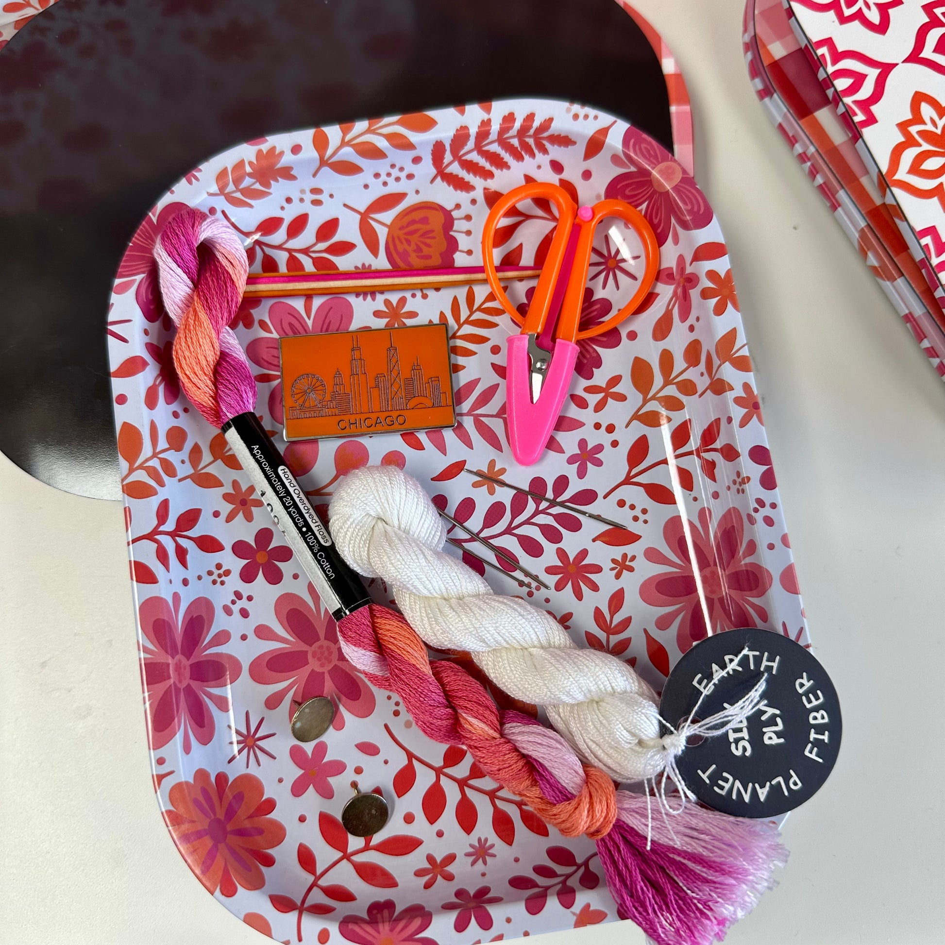 Crafting tools including yarn, scissors, and a needle on a floral-patterned tray.