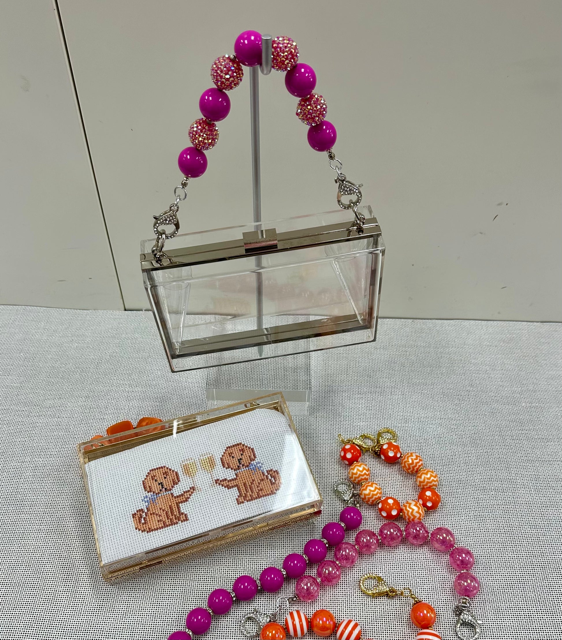 Clear handbag with pink and orange beaded accessories on a light gray surface.
