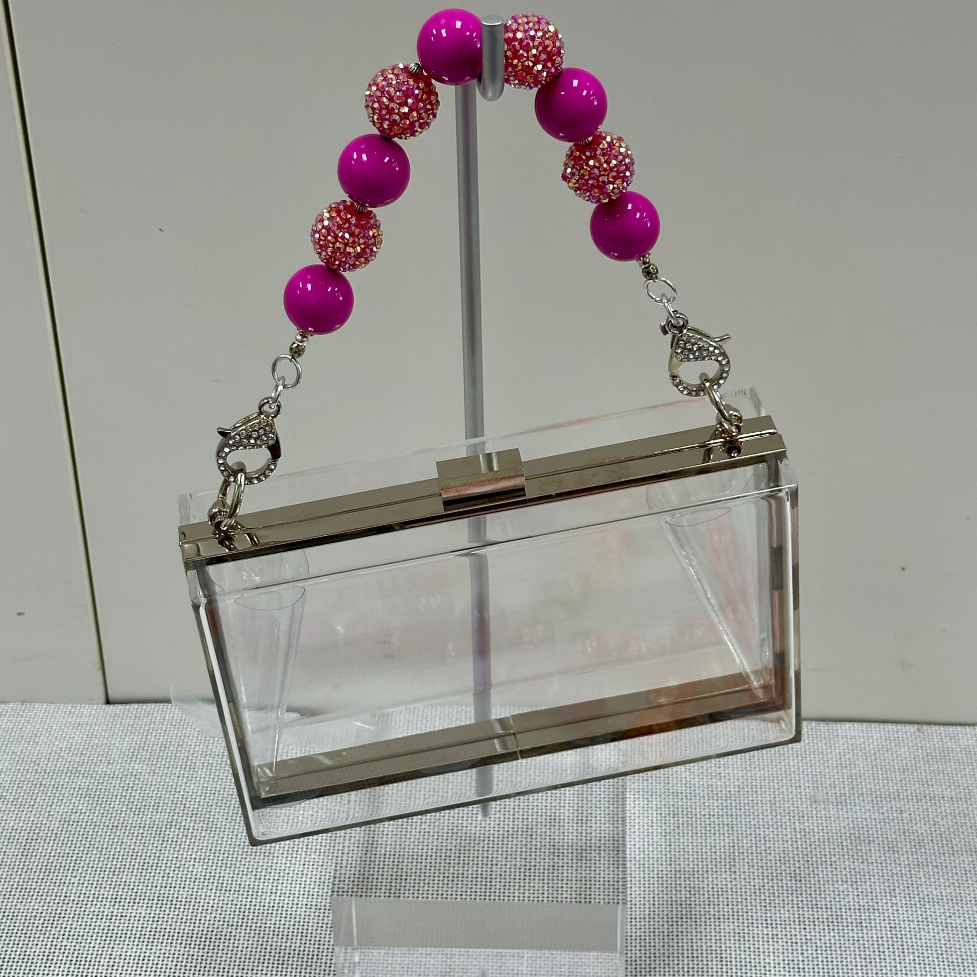 Clear handbag with a pink beaded strap on a neutral background