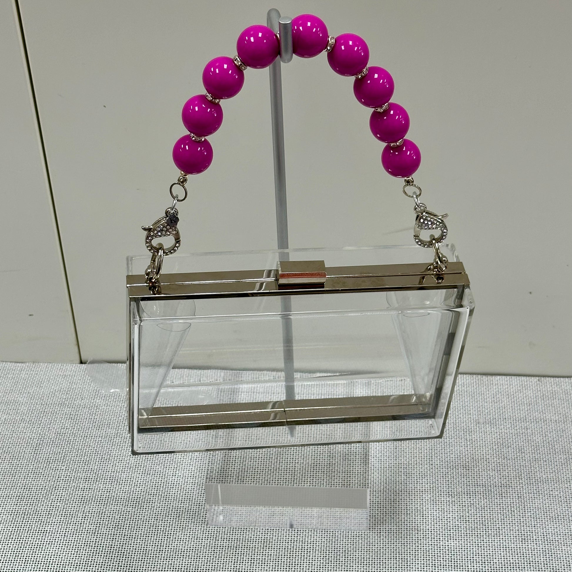 Clear handbag with pink beaded handle on a neutral background