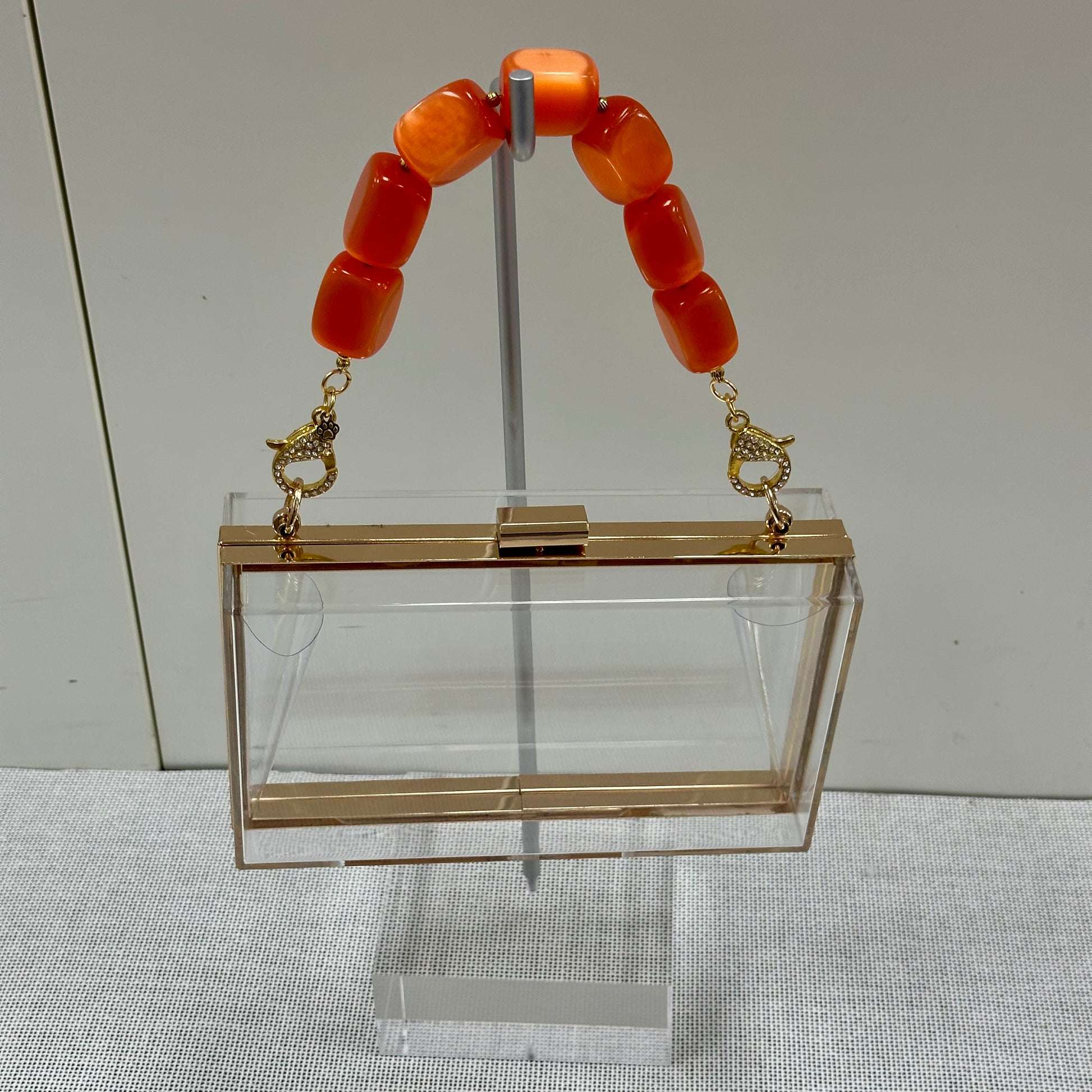 Clear handbag with gold handle and orange beads on a gray surface