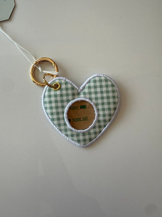 Heart-shaped fabric tag with green and white gingham pattern and gold ring