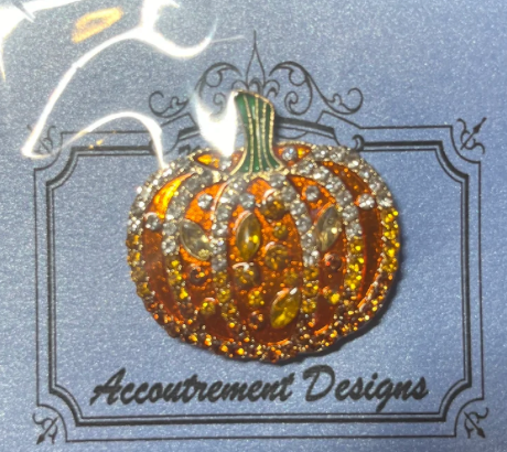 Pumpkin-shaped brooch with rhinestones on a card with 'Accoutrement Designs' branding.