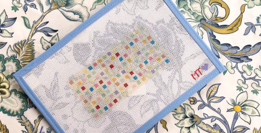 Cross-stitch pattern on aida fabric with a blue frame on a decorative floral background