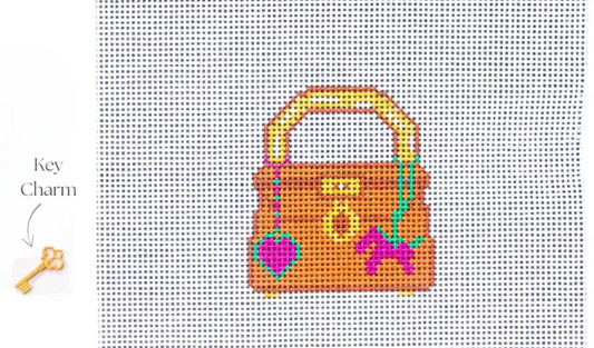 Cross-stitched design of a handbag with key charm on a grid background
