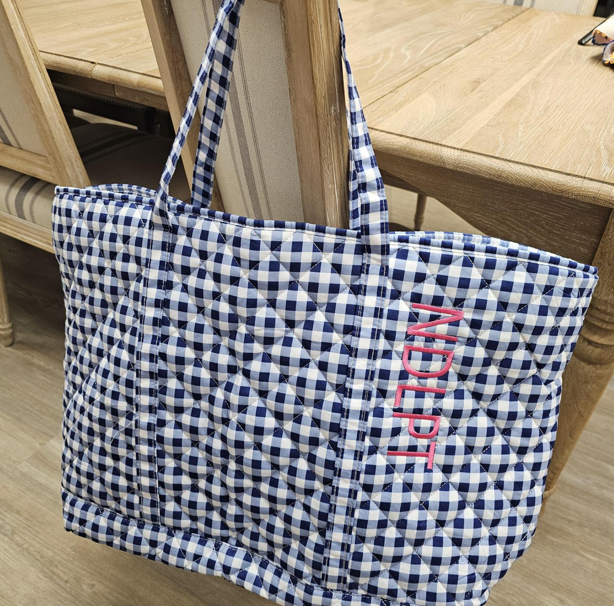 Blue and white checkered tote bag with 'Ninety' embroidery on a wooden floor.